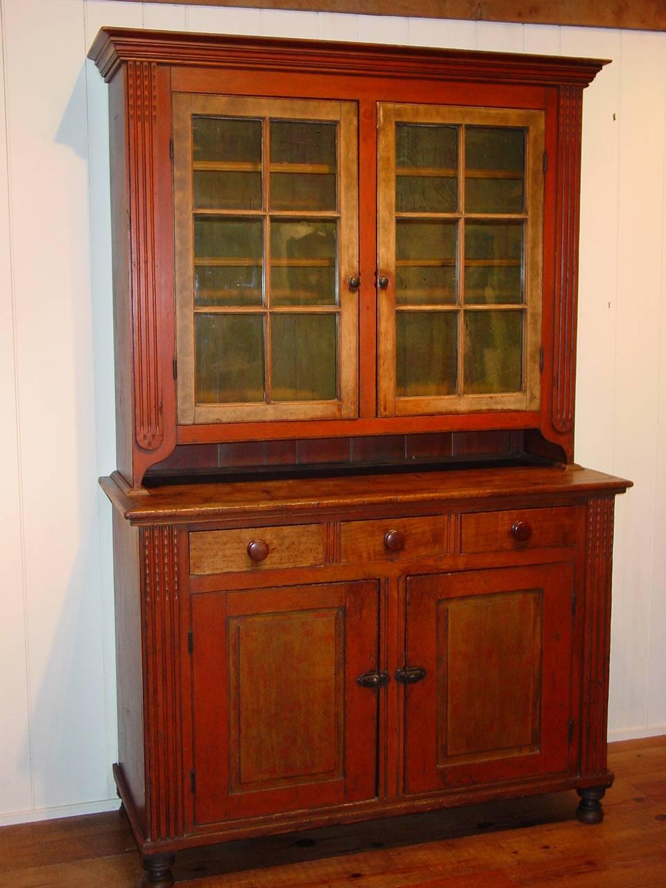 A Pennsylvania pine two-part Dutch cupboard retaining its original red-painted finish with yellow smoke-decorated doors and yellow interior. This Dutch cupboard, from Lancaster, Pennsylvania, is further distinguished by the gouge carved pilasters