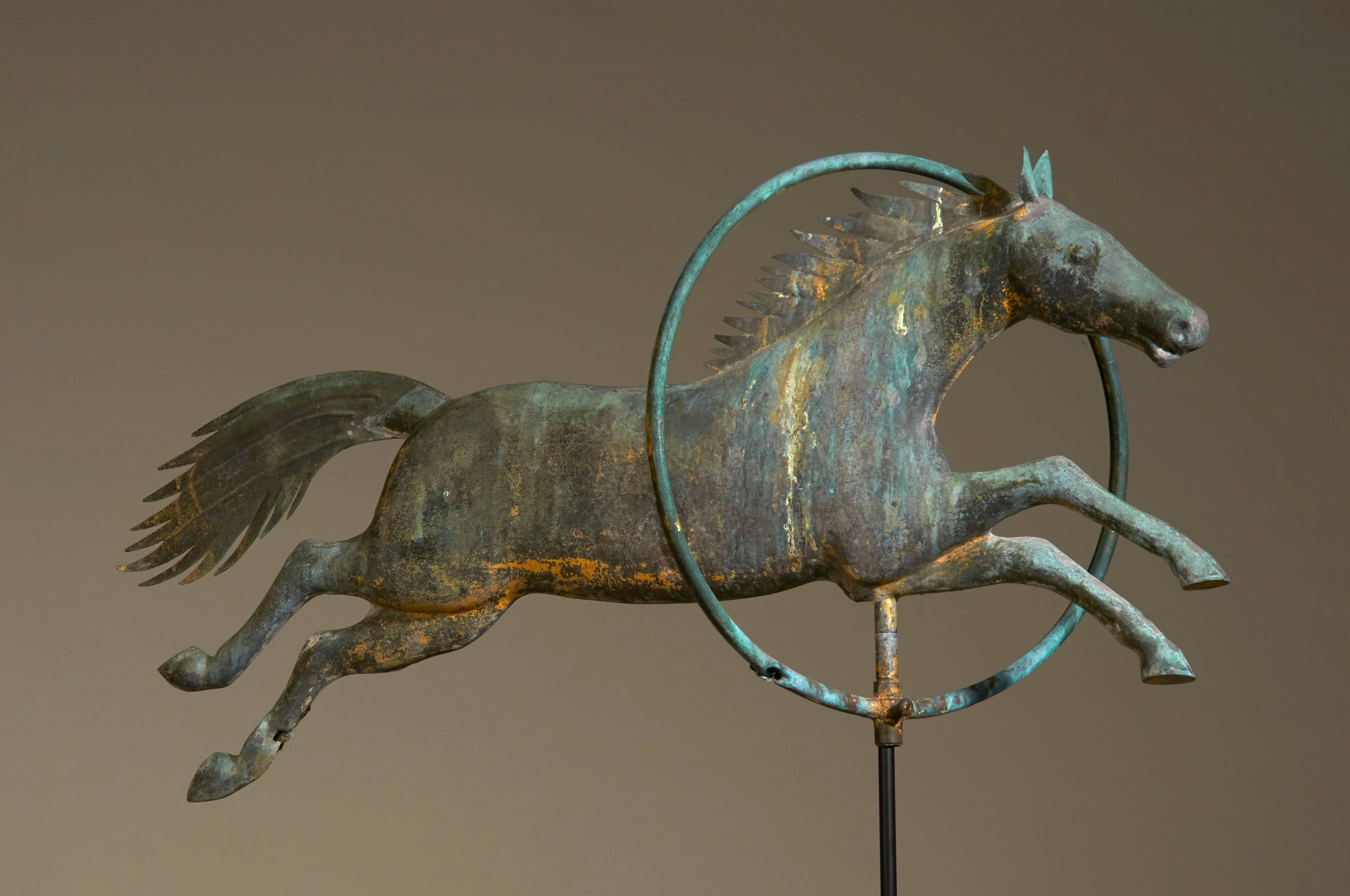 Attributed to A. L. Jewell & Co. (1852-1867) of Waltham, Massachusetts, this molded copper weathervane of a flattened full-body horse jumping through a hoop is a superlative example of a rare form. It retains a fine Verdigris surface showing
