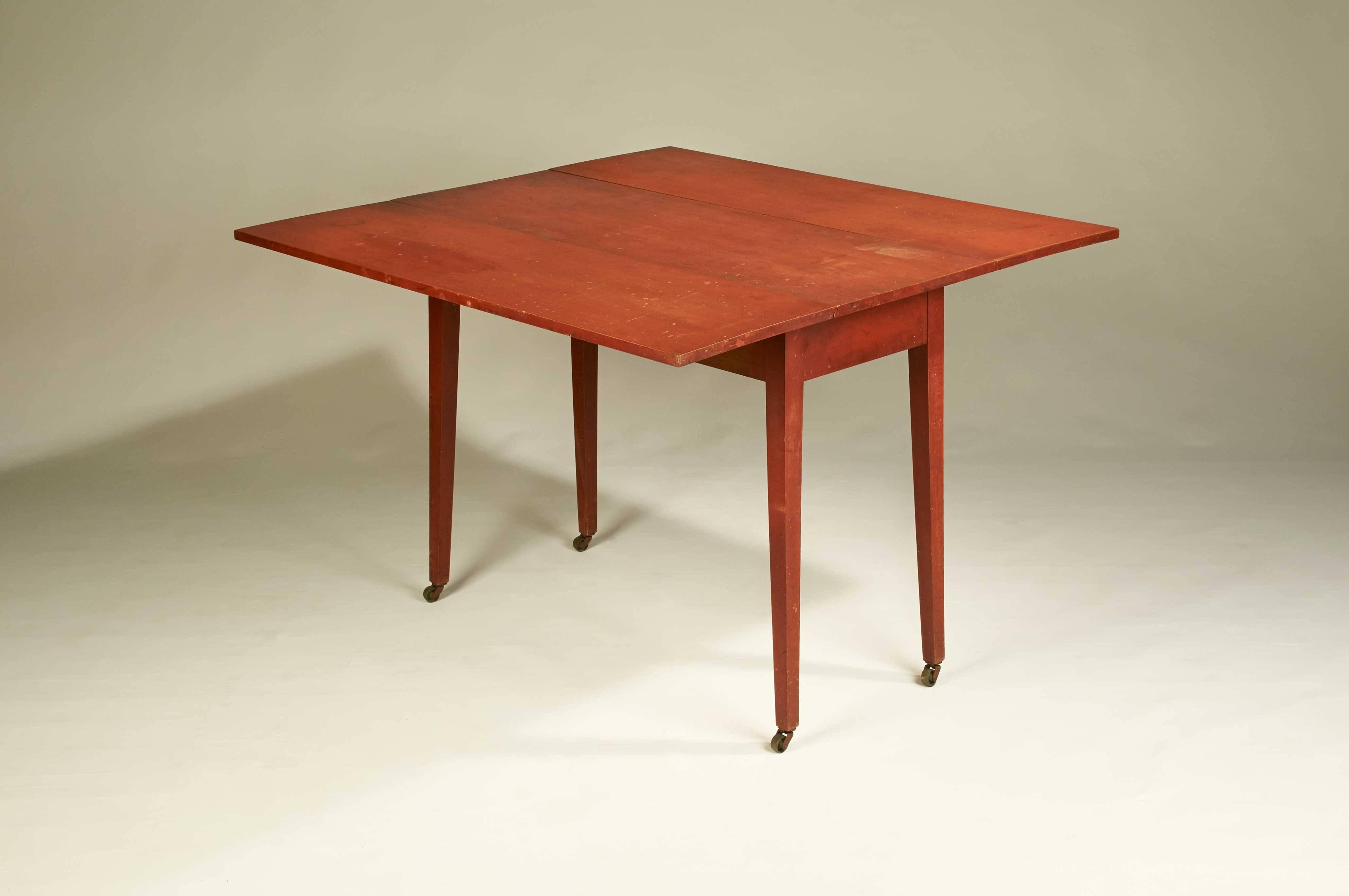 A New England country drop-leaf table with original red-painted surface over a maple frame. Legs are tiger maple.