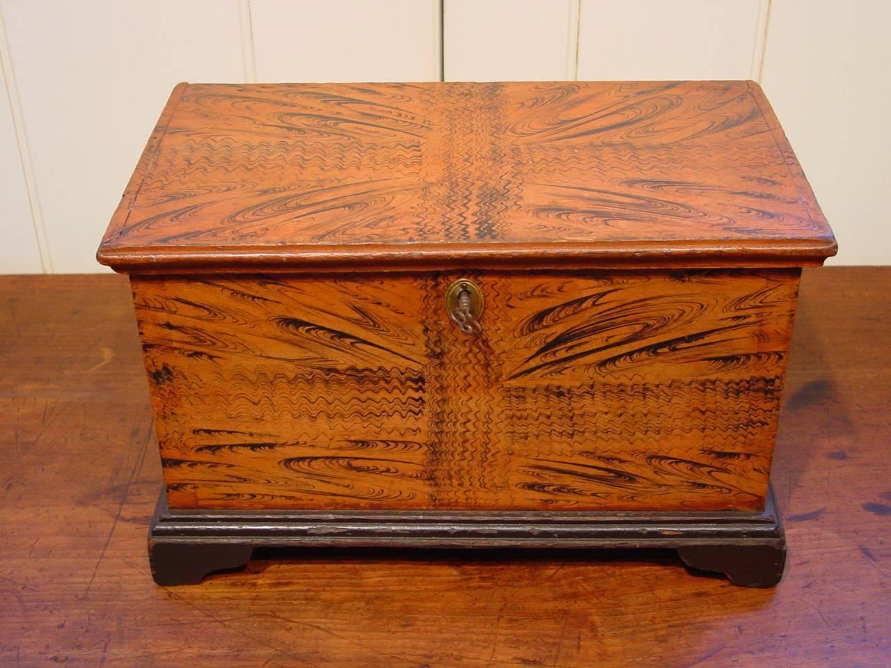 A pine miniature blanket chest from south-eastern Pennsylvania featuring exceptional grain-painted decoration simulating a ribbon tied around it. Additionally, this miniature blanket chest was expertly constructed with precise dovetailed joints and