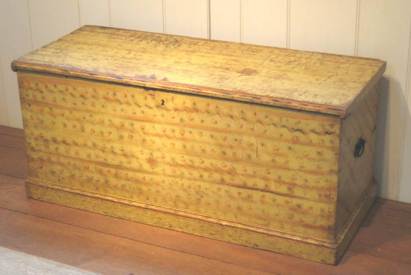 A New England pine chest with original red and black, dot and squiggle decoration on a yellow ground. This country chest also features a mold base with two iron handles and an interior till with drawer.