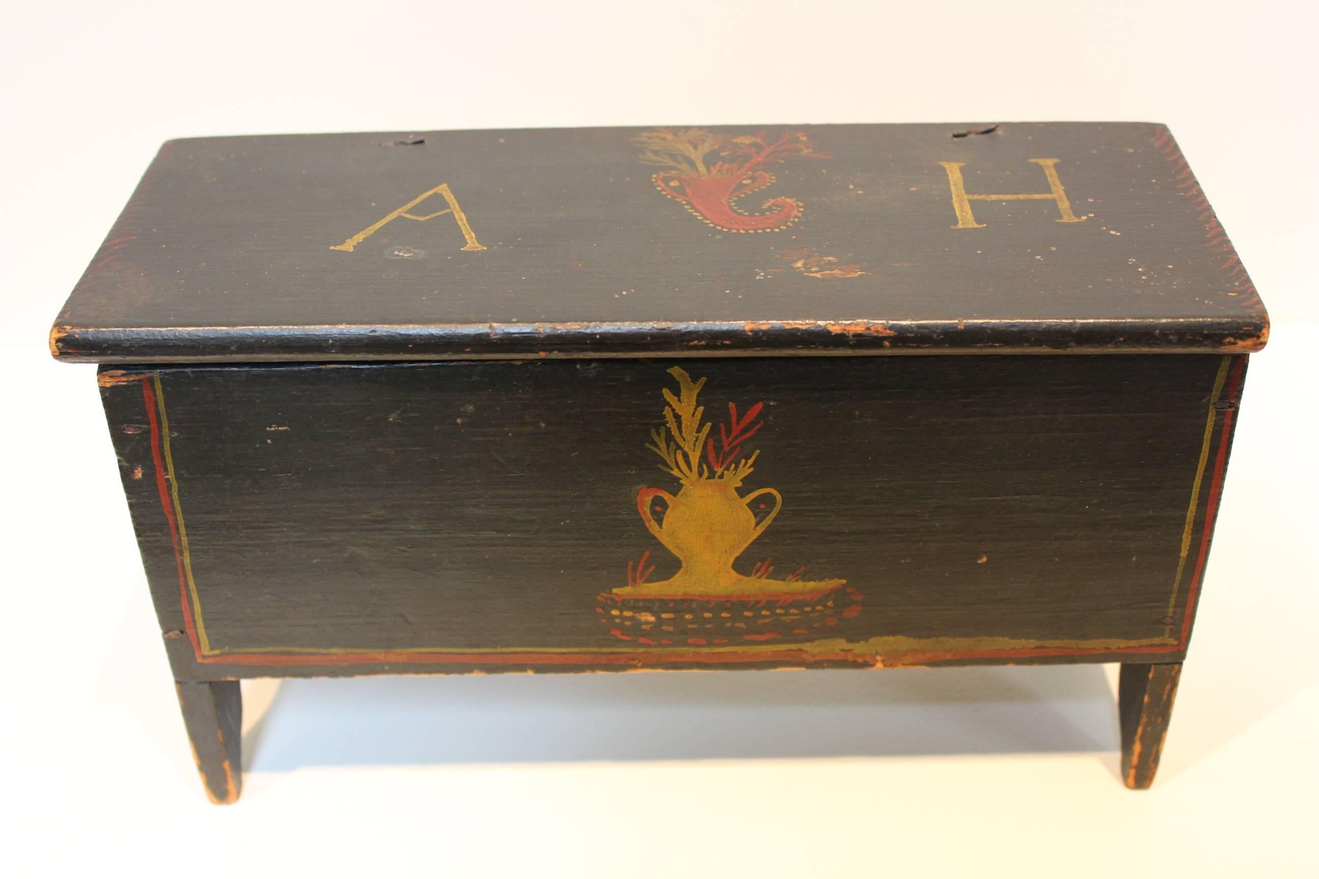 A charming New England miniature blanket chest constructed of pine with original yellow and red polychrome decoration on a dark blue navy ground. The lift-top lid bears the initials 'AH'.