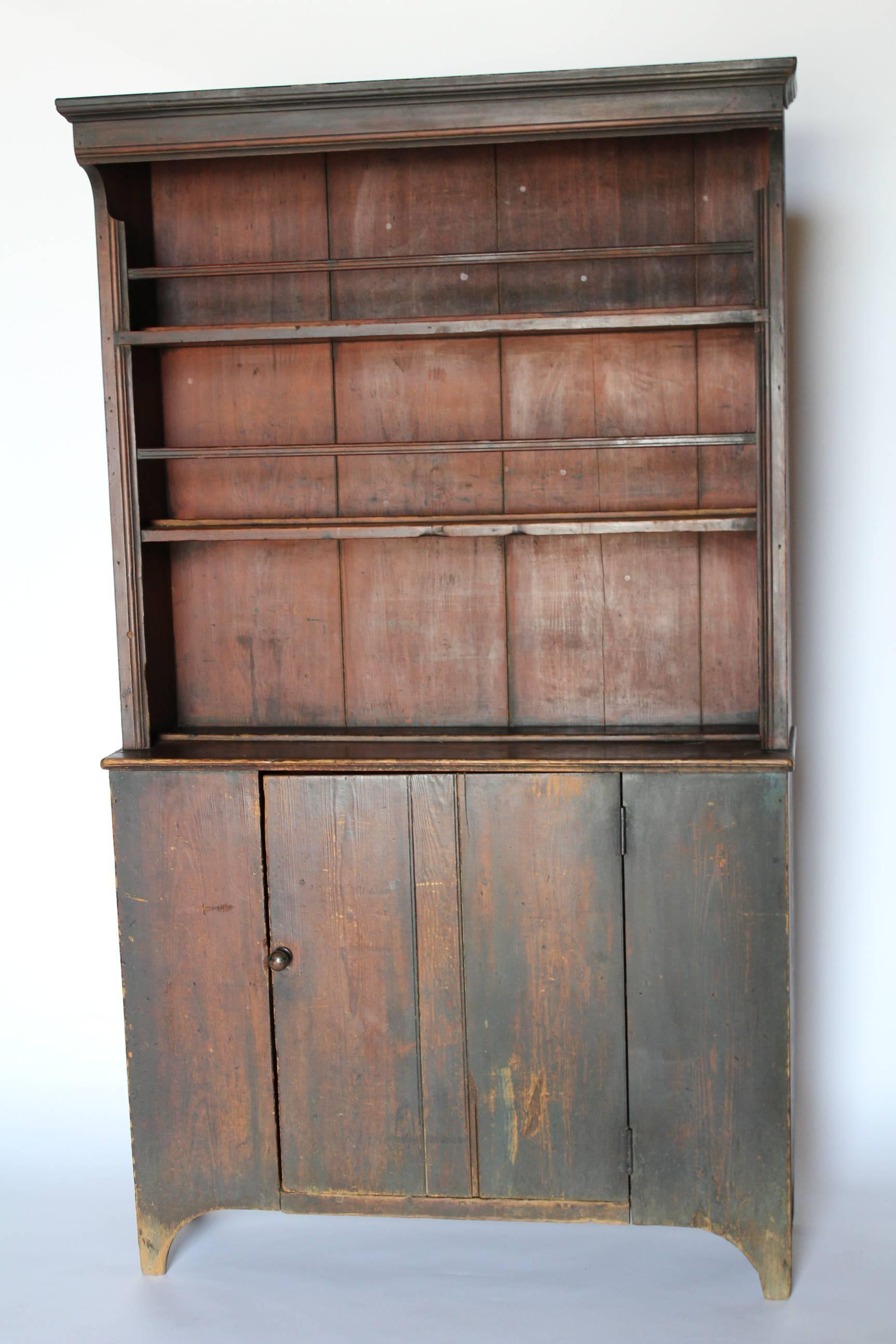 A Southern step-back cupboard of pleasing proportions featuring a rare, hooded cornice top. This cupboard is constructed of long-grain Southern pine and retains its original blue-painted exterior, which has darkened over time, and red-painted