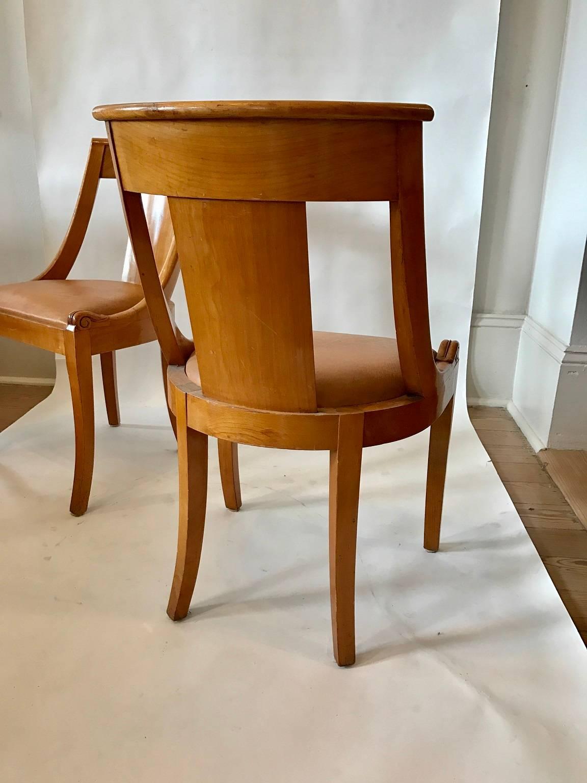 Eight fruitwood dining chairs in the Biedermeier taste; curved backs and saber front legs; leather upholstery at the slip seats, four shown.