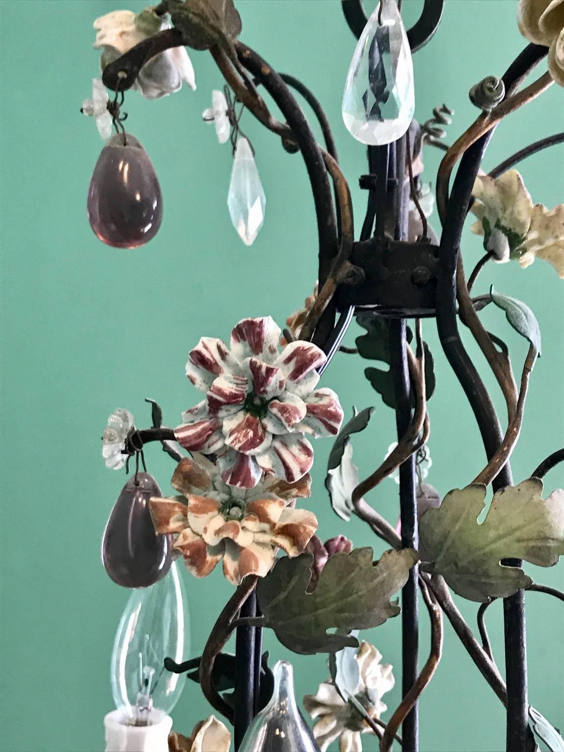 Charming four-light chandelier in iron adorned with leaves in tole-paint; the porcelain flowers in shades of ivory, blue and lavender; the drops in faceted and cabochon crystal both clear and lavender.