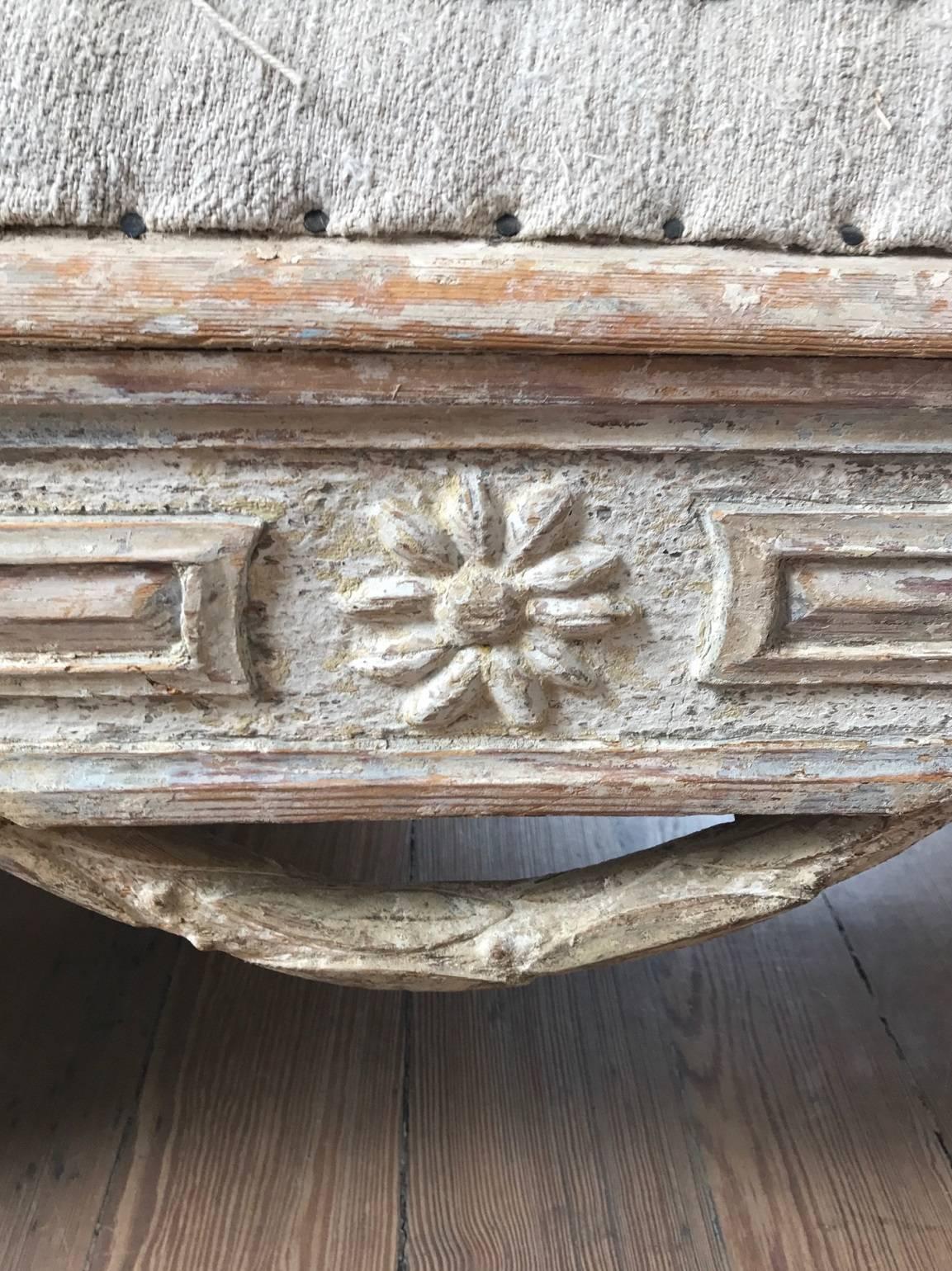 Early 19th century Gustavian three-seat sofa; the frame with attractive carvings in high relief; raised panels, rosettes and unusual foliate swags at the seat rail; the arm rests carved with stylized urns and vines; fluted square tapering legs;