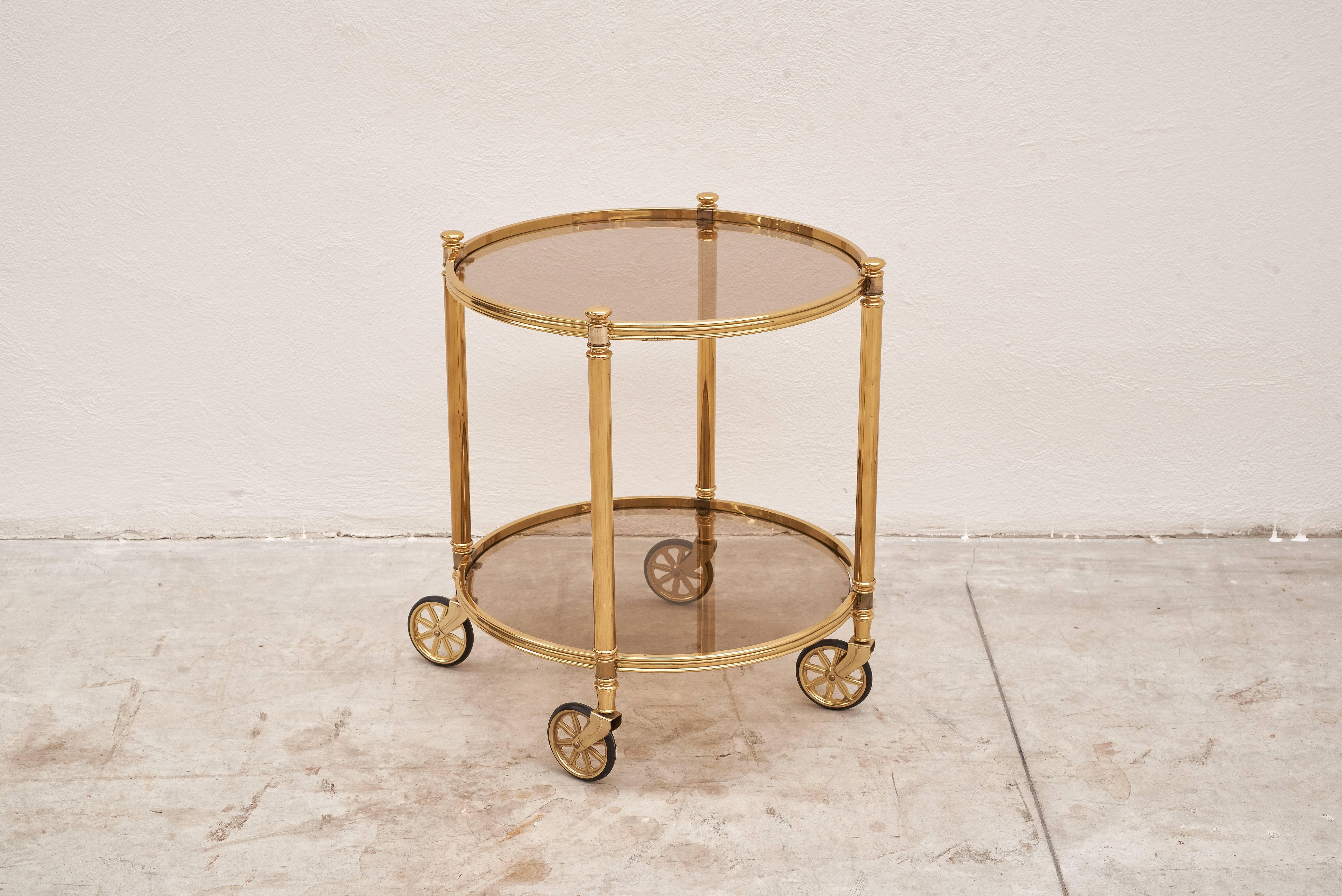 1970s Italian two-tier circular brass bar cart with smoked glasses. 

Very good condition with pleasant patina on metal part.