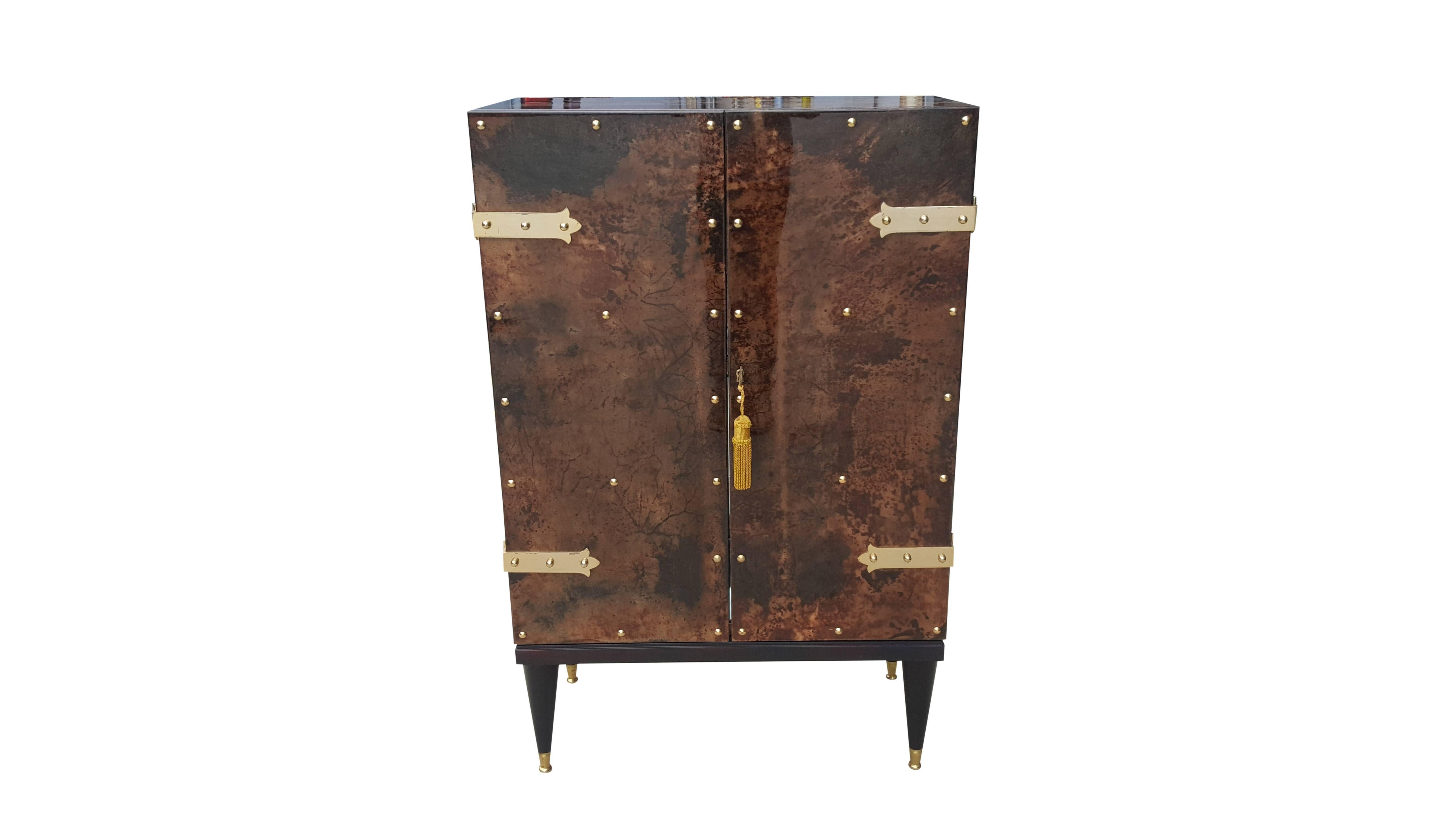 This two door dry-bar cabinet make for an ease of accessibility to the interior which is fitted with glass shelves. 
The middle shelf is horse-shoe shaped for taller bottles.
 Mahogany and brass legs, lacquered goatskin.

This is definitely the