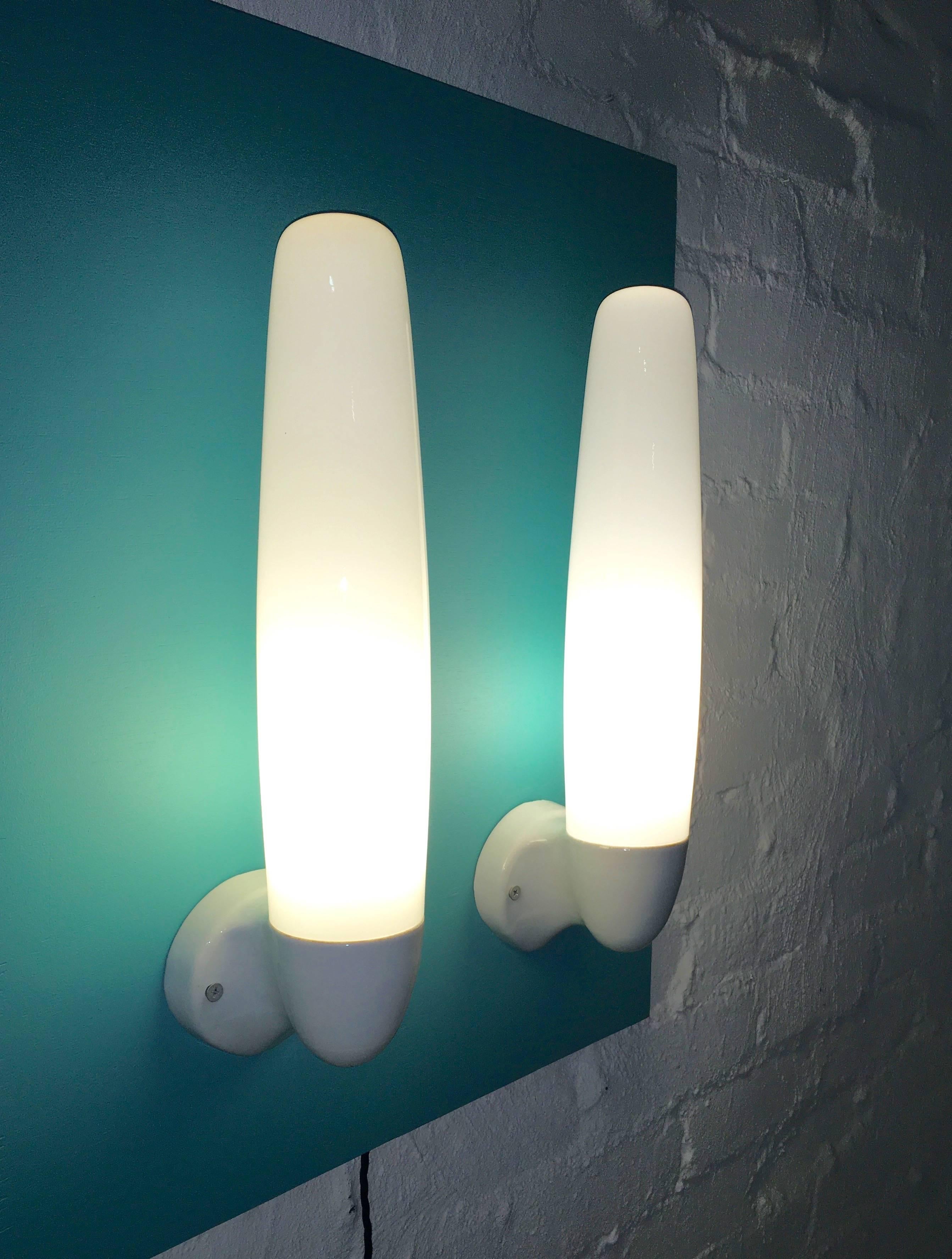 Fabulous prize winning wall lights designed in 1955 by Wilhelm Wagenfeld for Lindner Leuchten, Bamberg, Germany. 

Porcelain fixture and fittings with tall milk glass shade and threaded closure. One in perfect condition, one with small nibbles on