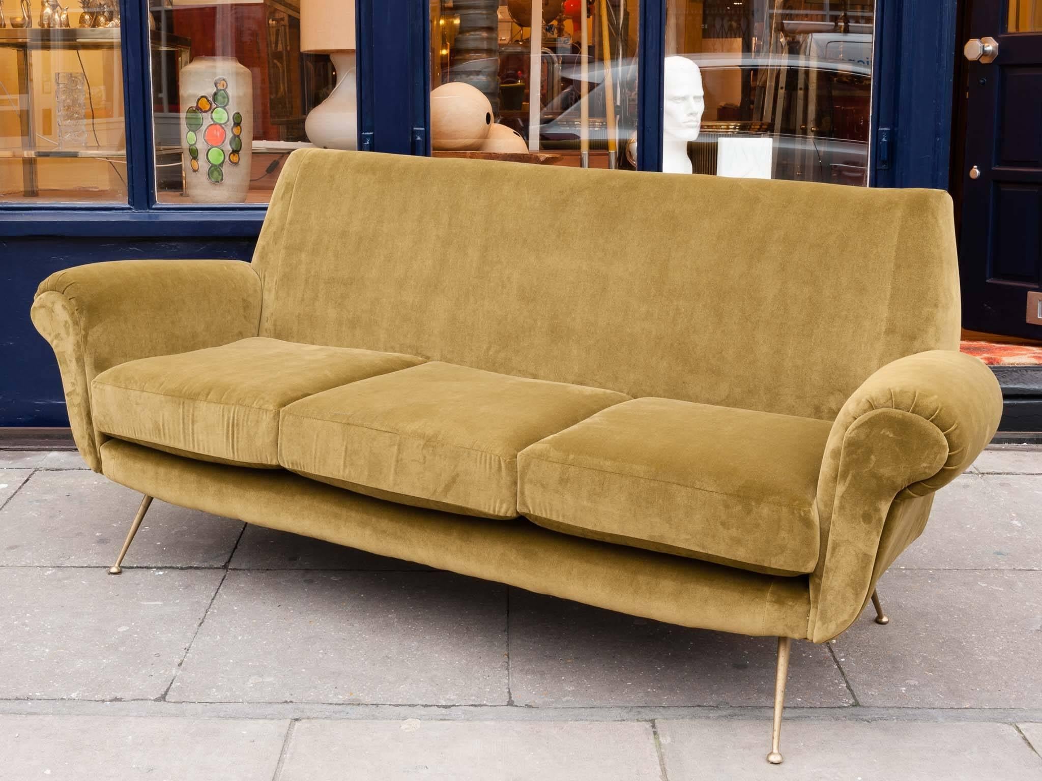 Midcentury 1950s three-seat Italian sofa, with four brass tapered feature legs. Newly upholstered in a moss green deep velvet fabric with three removable cushions. Elegant, comfortable and functional. A wonderful sofa with curved arms and a deep