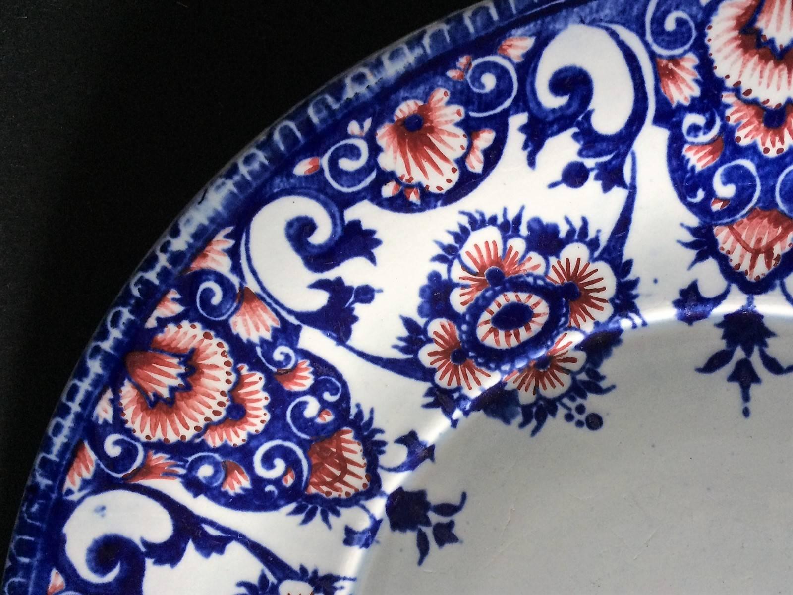 Dekorativer Steingutteller aus Gien, verziert mit blauen und roten stilisierten Blumenmotiven auf weißem Grund.
Stempel der Manufaktur von Gien auf der Rückseite des Tellers.