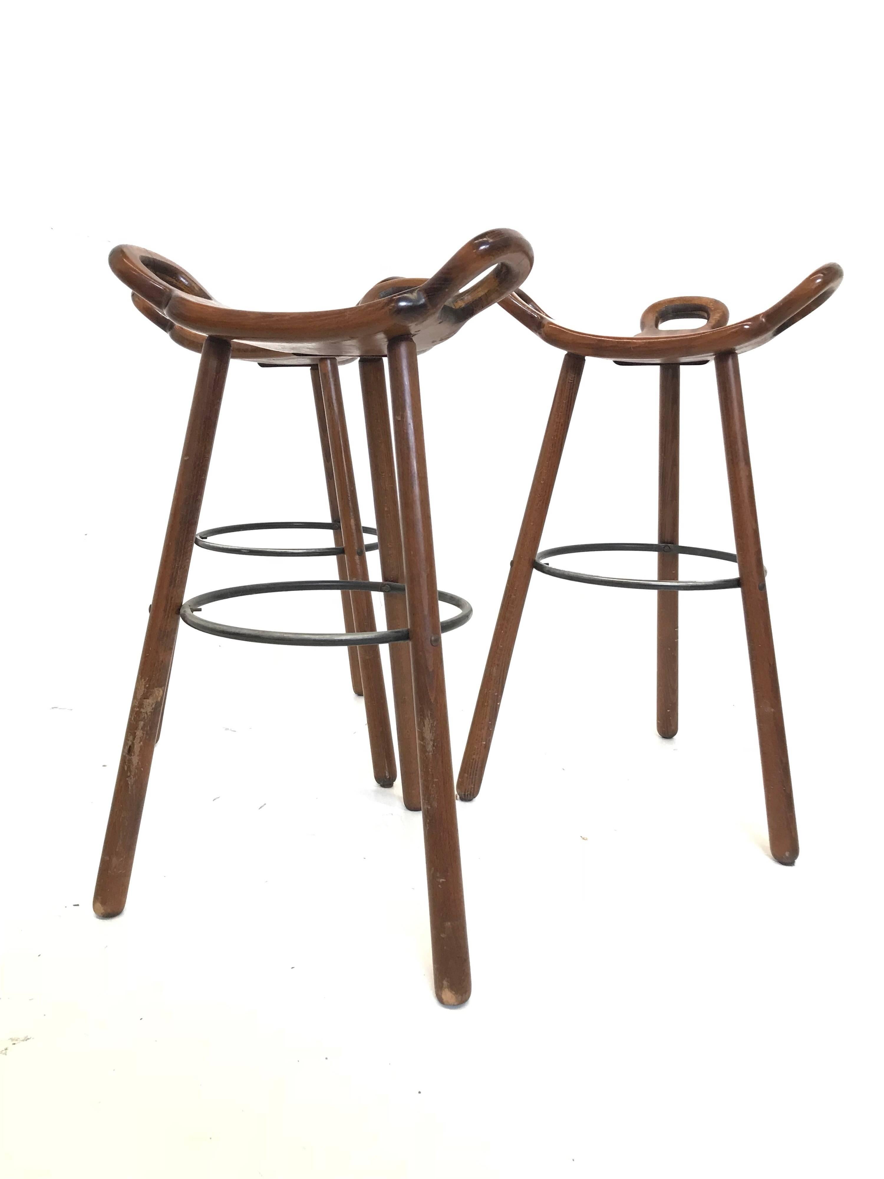 Set of three 'Brutalist' or 'Marbella' bar stools, in stained beech and metal, Spain, 1970s. A curved T-shape with three handles. The curved form makes sure the stool has a stabile seat, emphasized by the metal ring as footrest. These bar stools are