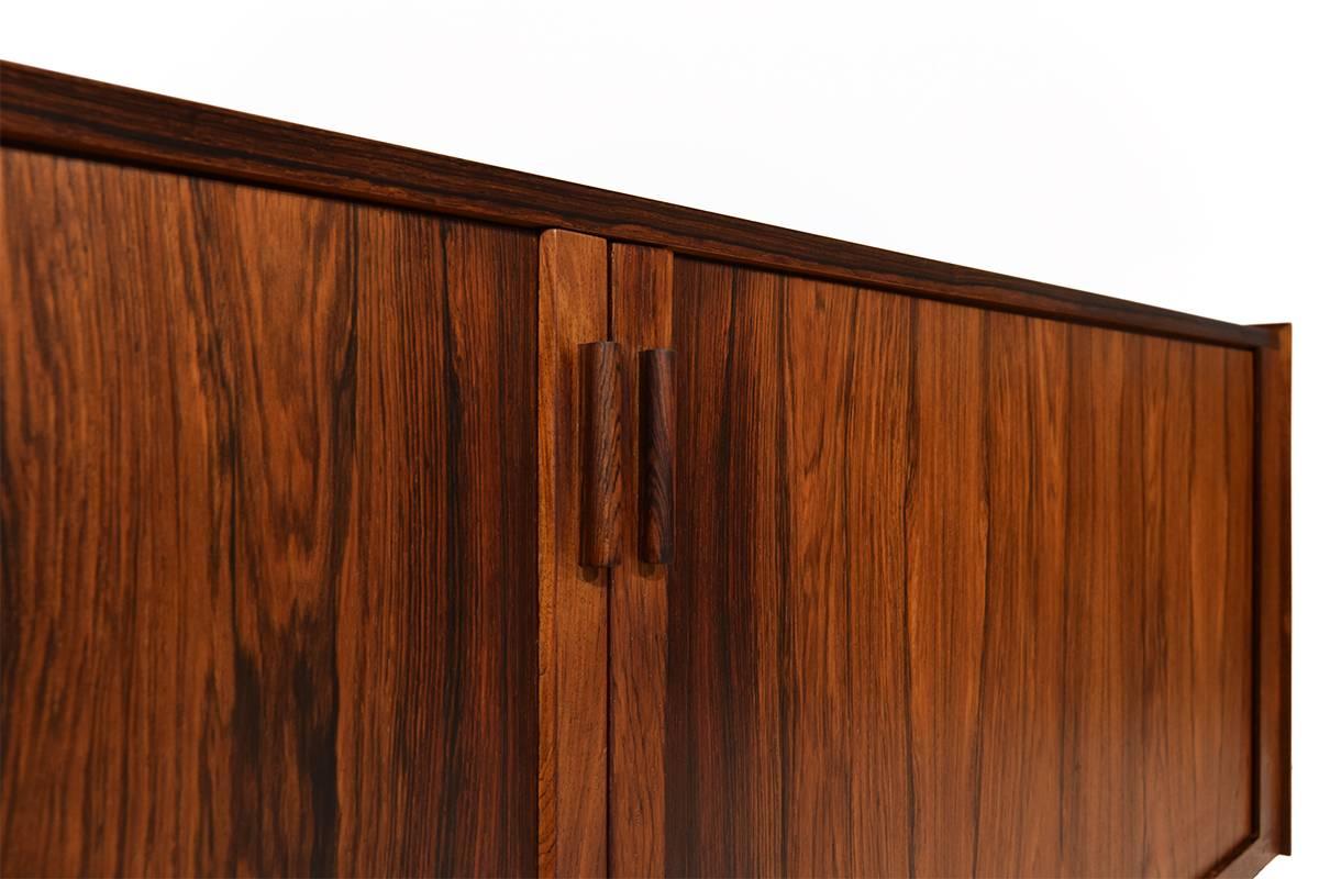 This marvellous credenza was designed by the famous Ib Kofod-Larsen. It is made from rosewood and features tambour sliding doors and four sliding drawers. This credenza can be positioned against a wall or can be positioned freestanding. The rosewood