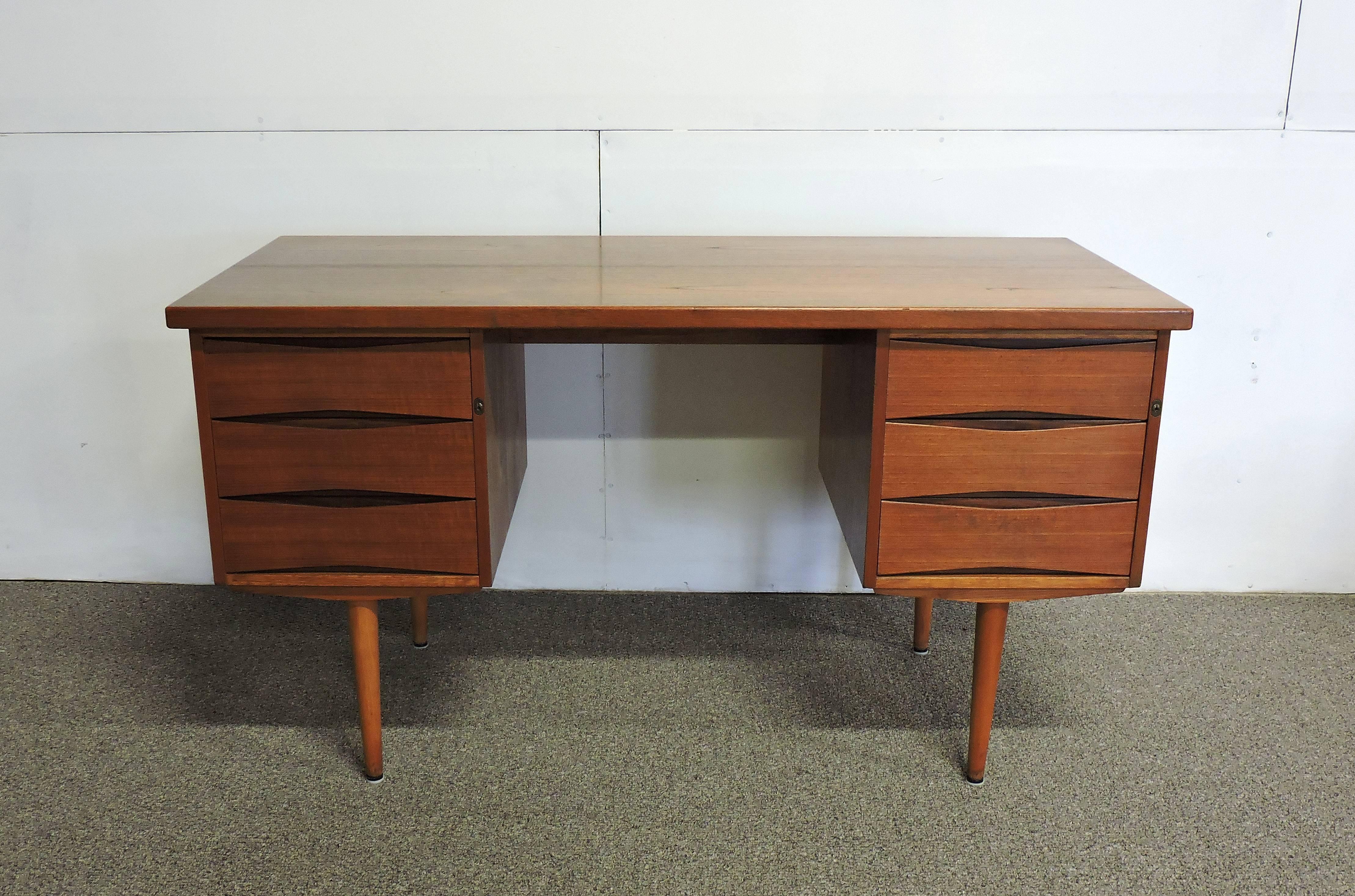 Handsome desk attributed to Arne Vodder and made in Denmark. This desk has a single file cabinet drawer on the right, and three drawers on the left. Both sides lock, and the original key is included. Beautiful eye-shaped recessed pulls and tapered