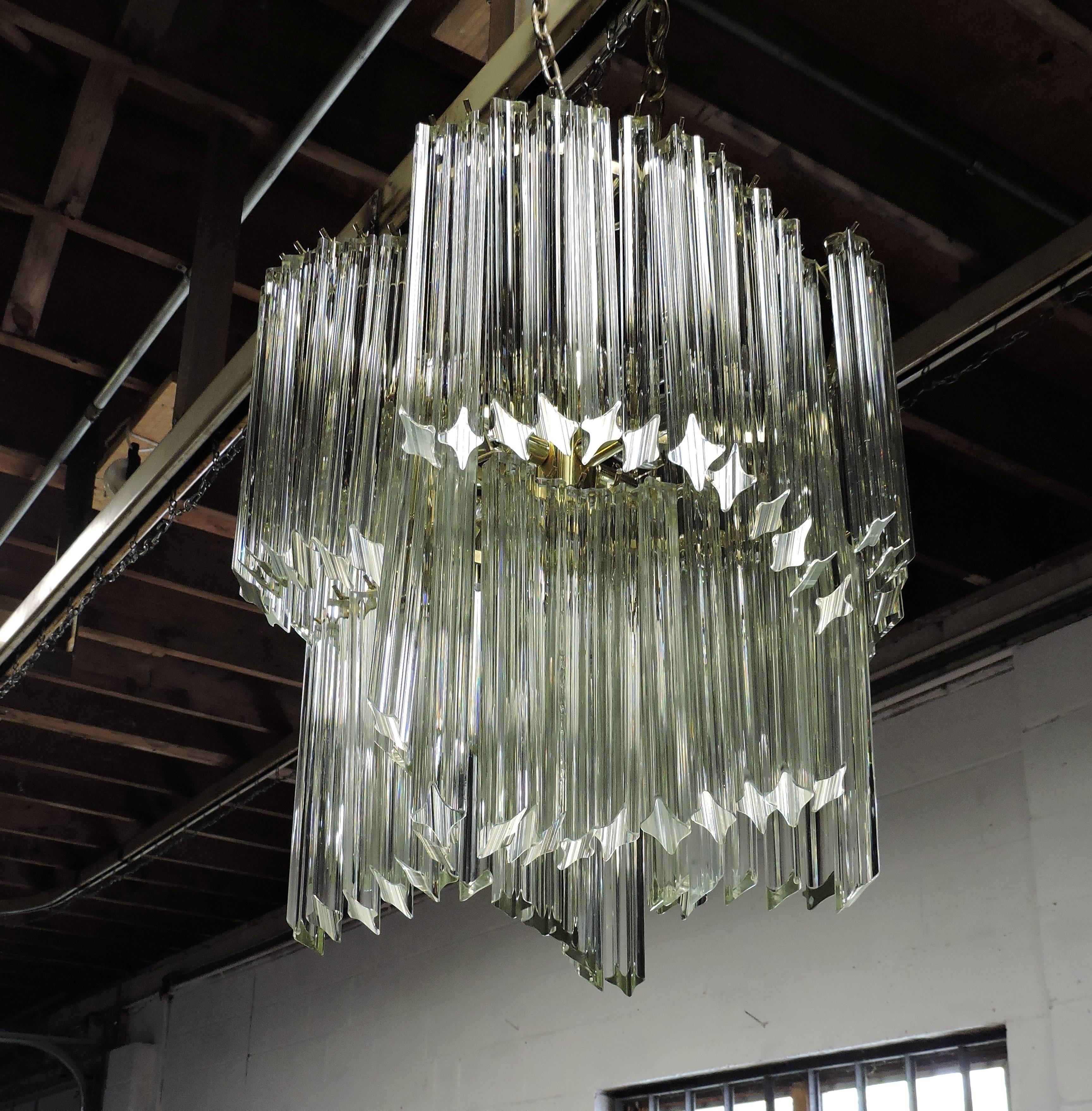 Stunning quatro punta glass prism chandelier. This chandelier has almost one- hundred angled prisms that hang in two tiers from a brass frame in an unusual curved pattern. It takes nine candelabra based bulbs and one standard base bulb. A ceiling