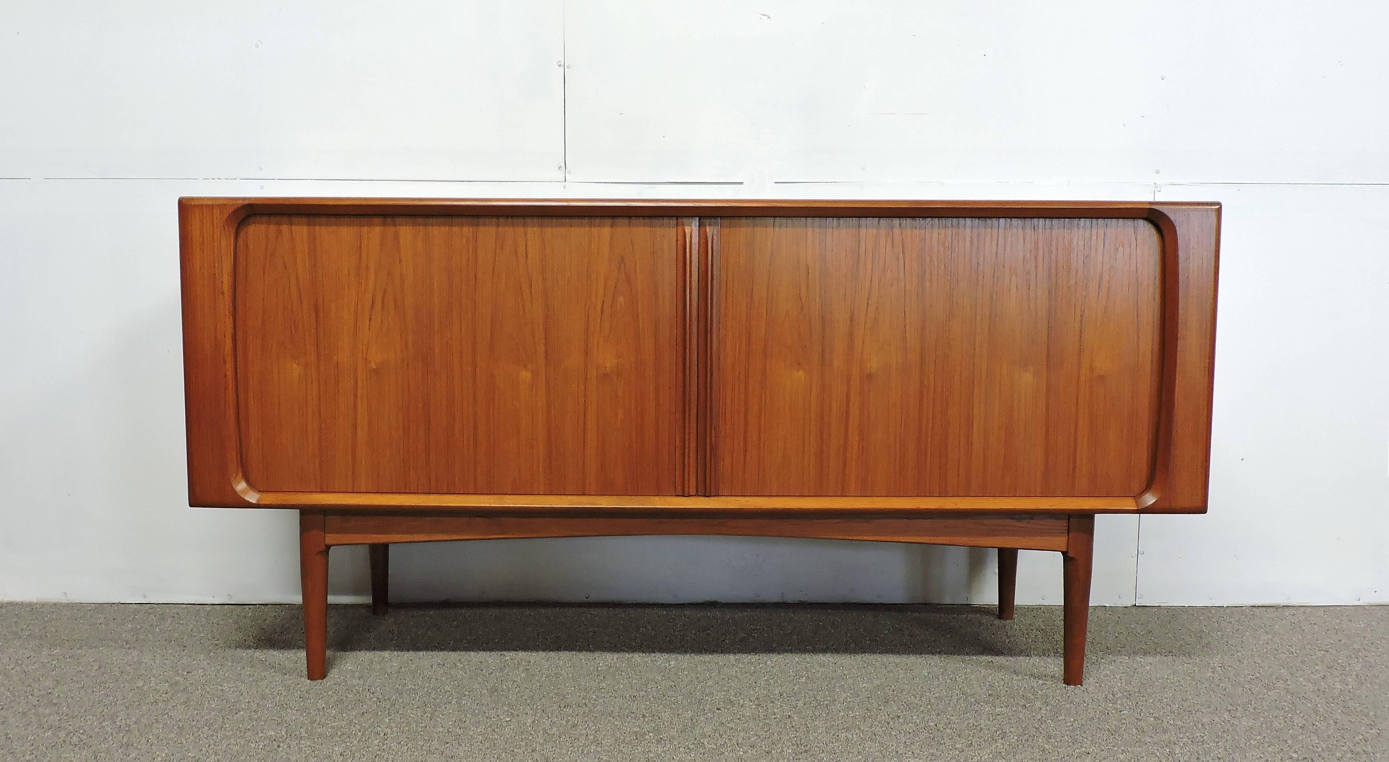 Handsome teak credenza, model 142/65, made in Denmark by Bernhard Pedersen and Son.
This high quality cabinet has tambour doors with sleek sculpted teak pulls which open to reveal three drawers and three adjustable shelves. It sits on tapered legs