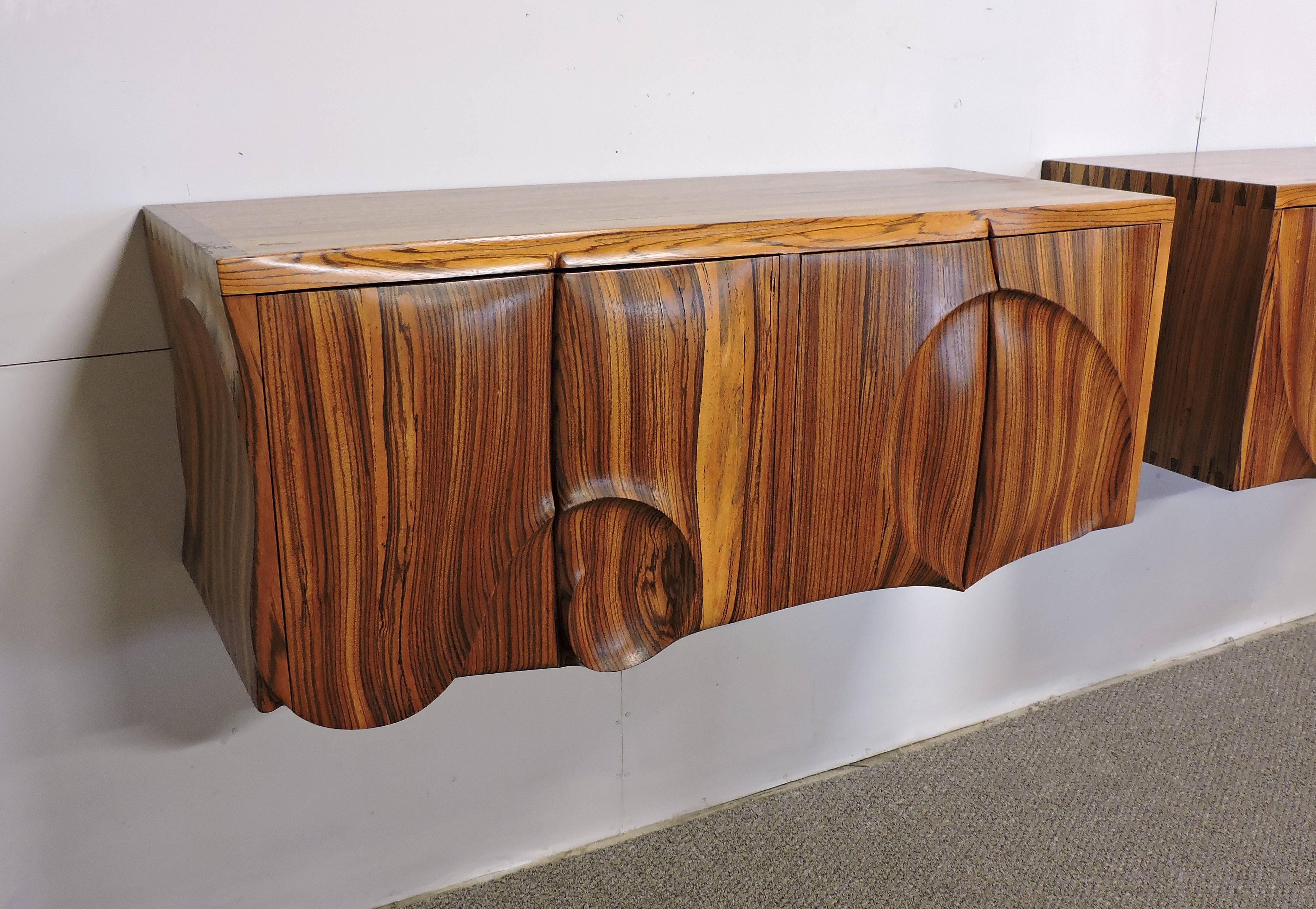 Truly unique and one-of-a-kind hanging cabinets made out of solid exotic zebra wood. These handmade cabinets have a striking look with curvaceous carved panels which nicely compliments the grain of the wood. The cabinet on the left has a pull-out