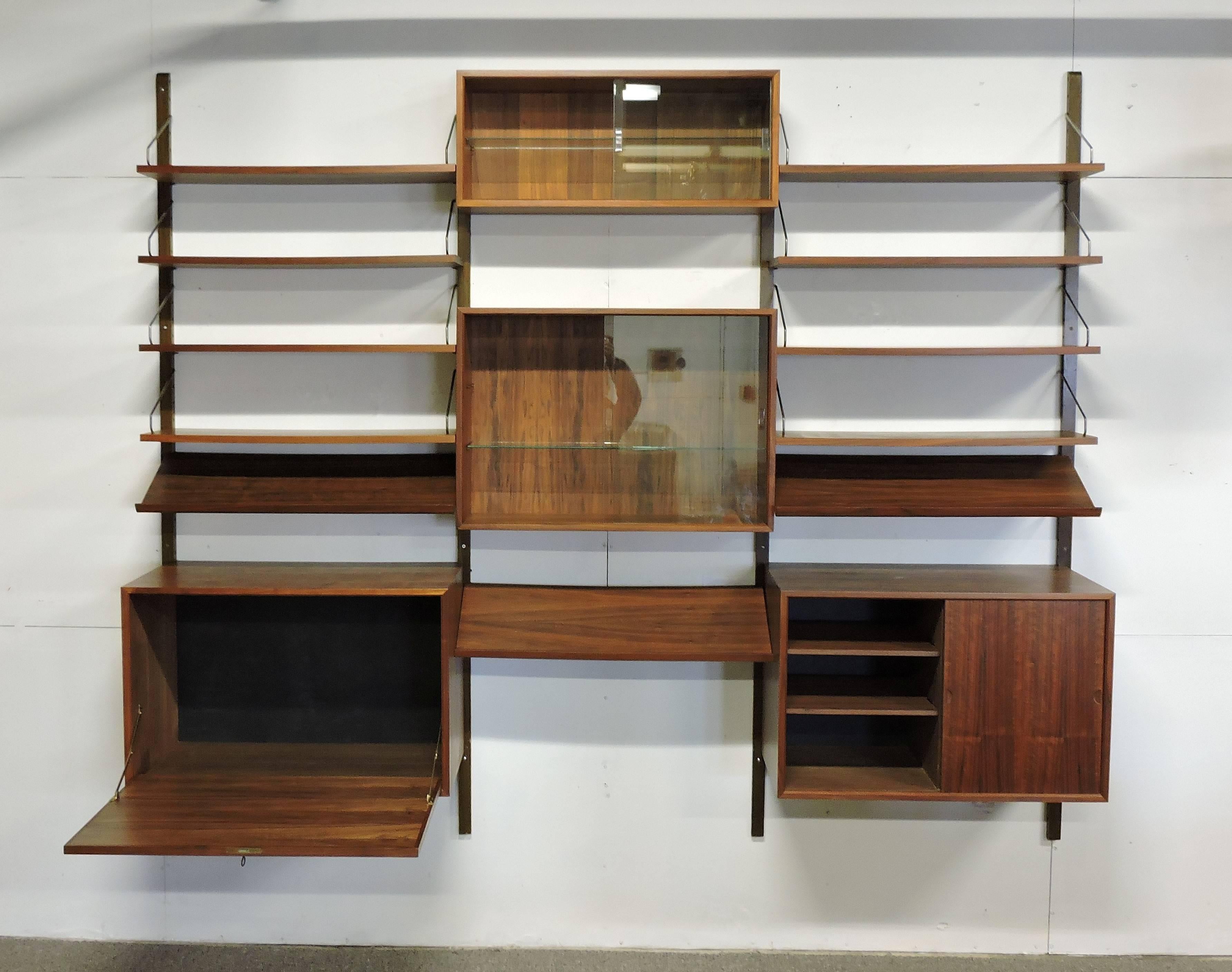 Large three bay Royal system wall unit designed by Poul Cadovius and made in Denmark. This unit includes four poles, four modules, eight shelves and three hard-to-find magazine shelves. Two of the cabinets have sliding glass doors, each with a
