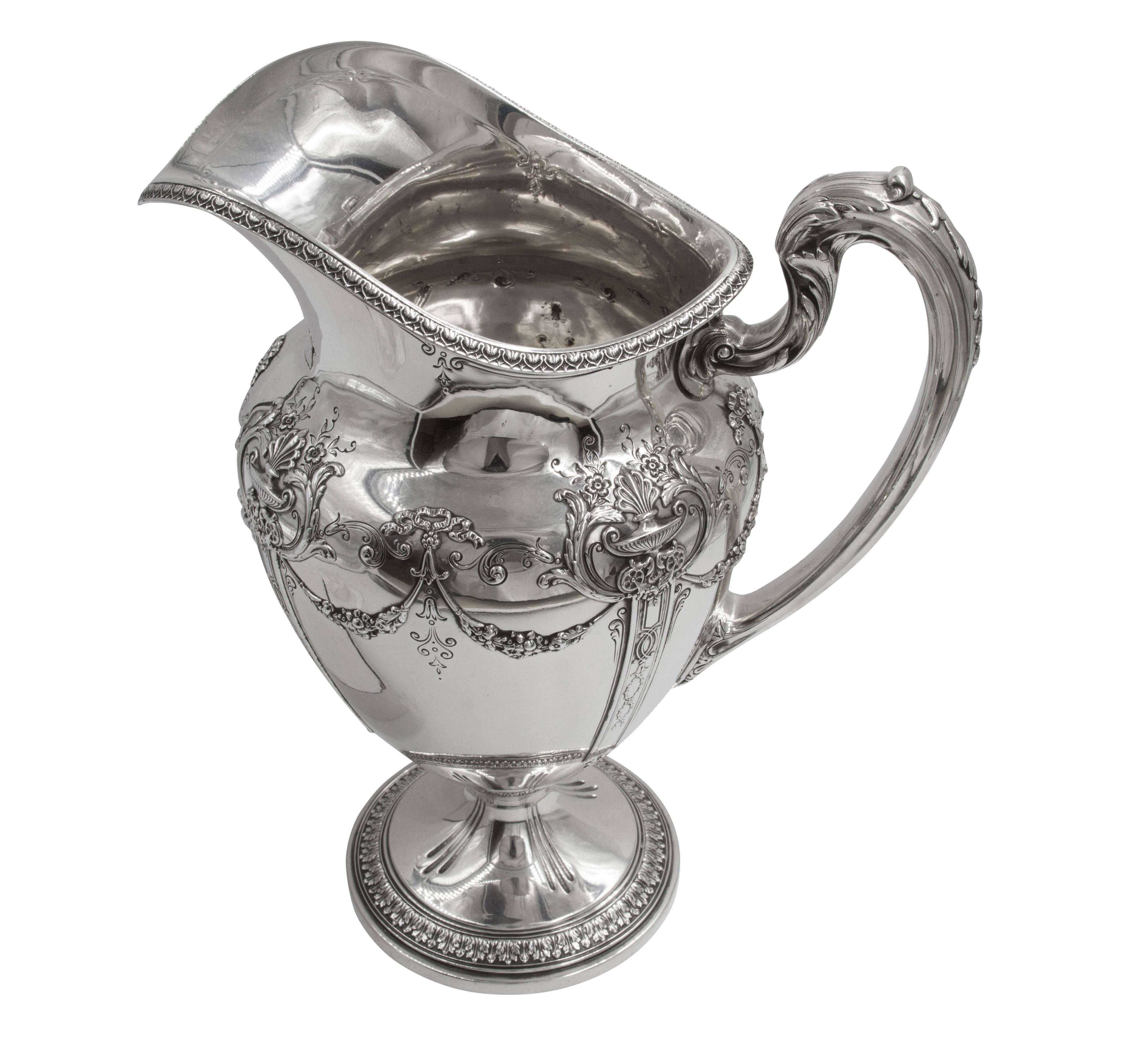This majestic water pitcher is sure to dress up any dinner table! Being offered is a Reed & Barton pitcher with garlands and bows adorning the entire top. The arched handle has a leaf-like pattern on both the side and top. The base has four groups