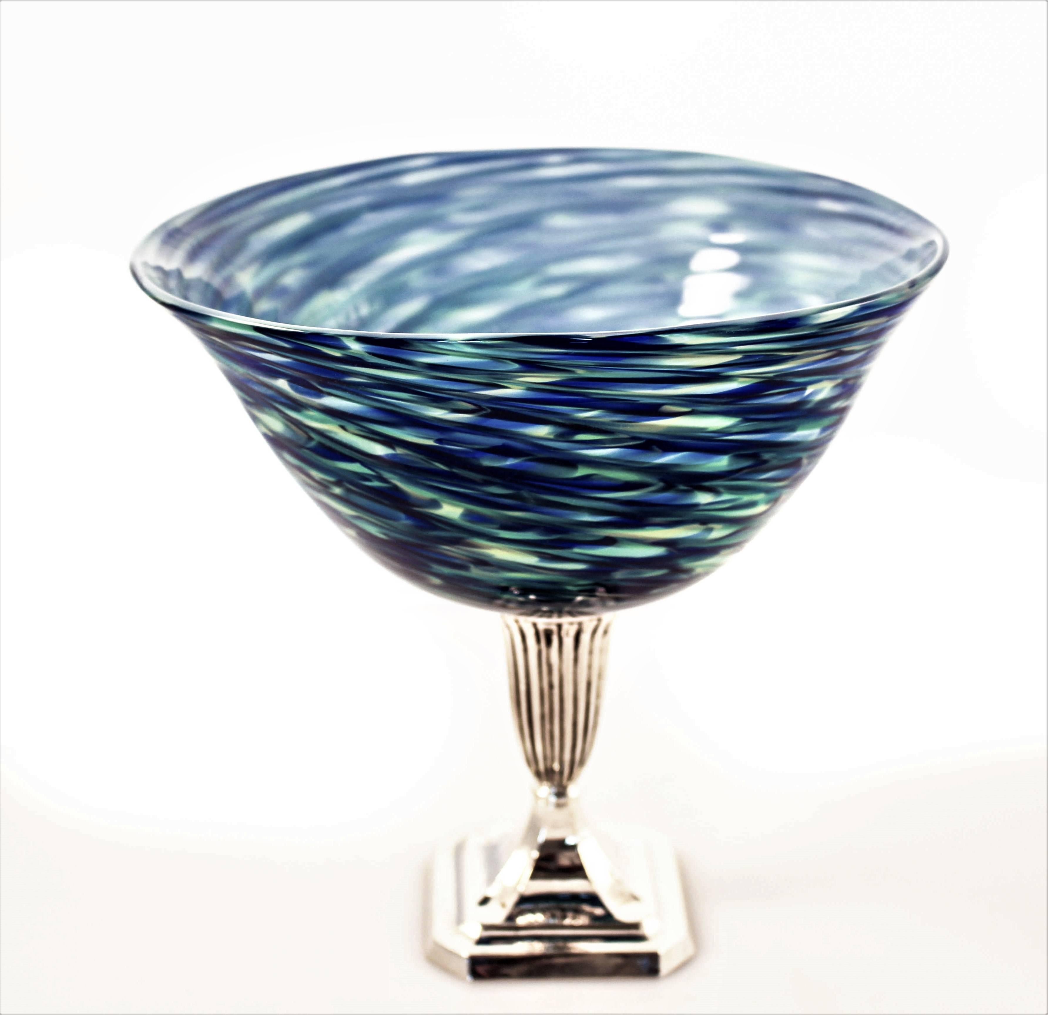 Different shades of blue, from light to dark with touches of pale yellow blend together in the glass like waves in an ocean. Sitting proudly on a sterling pedestal, this piece is great for practically anything you want to put inside. Or, leave it on