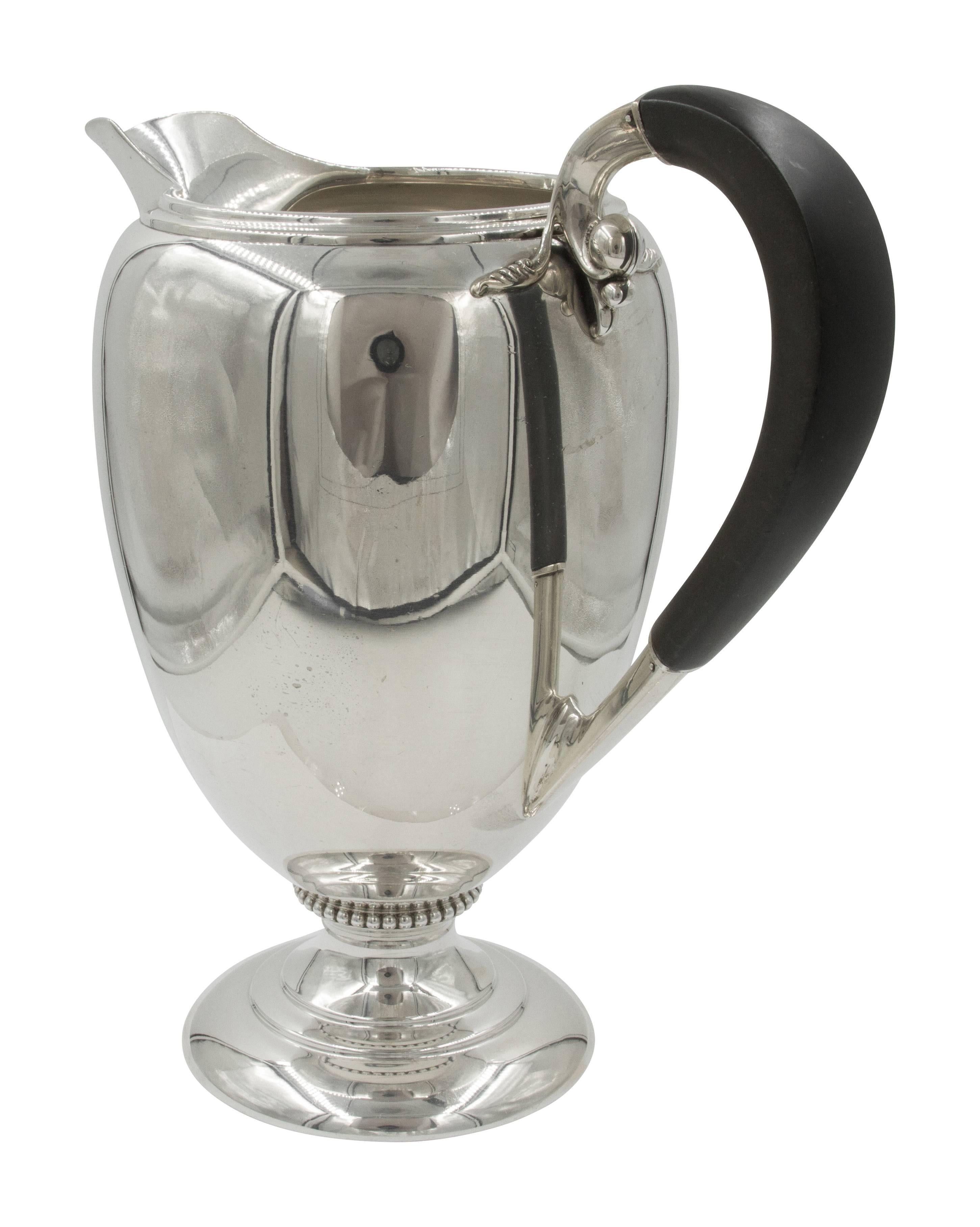 Art Deco water pitcher by Fisher Silversmiths. This handsome pitcher has a wood handle which immediately draws your attention to it. A ring of balls encircles the base and a larger ball is carefully placed where the handle meets the pitcher.