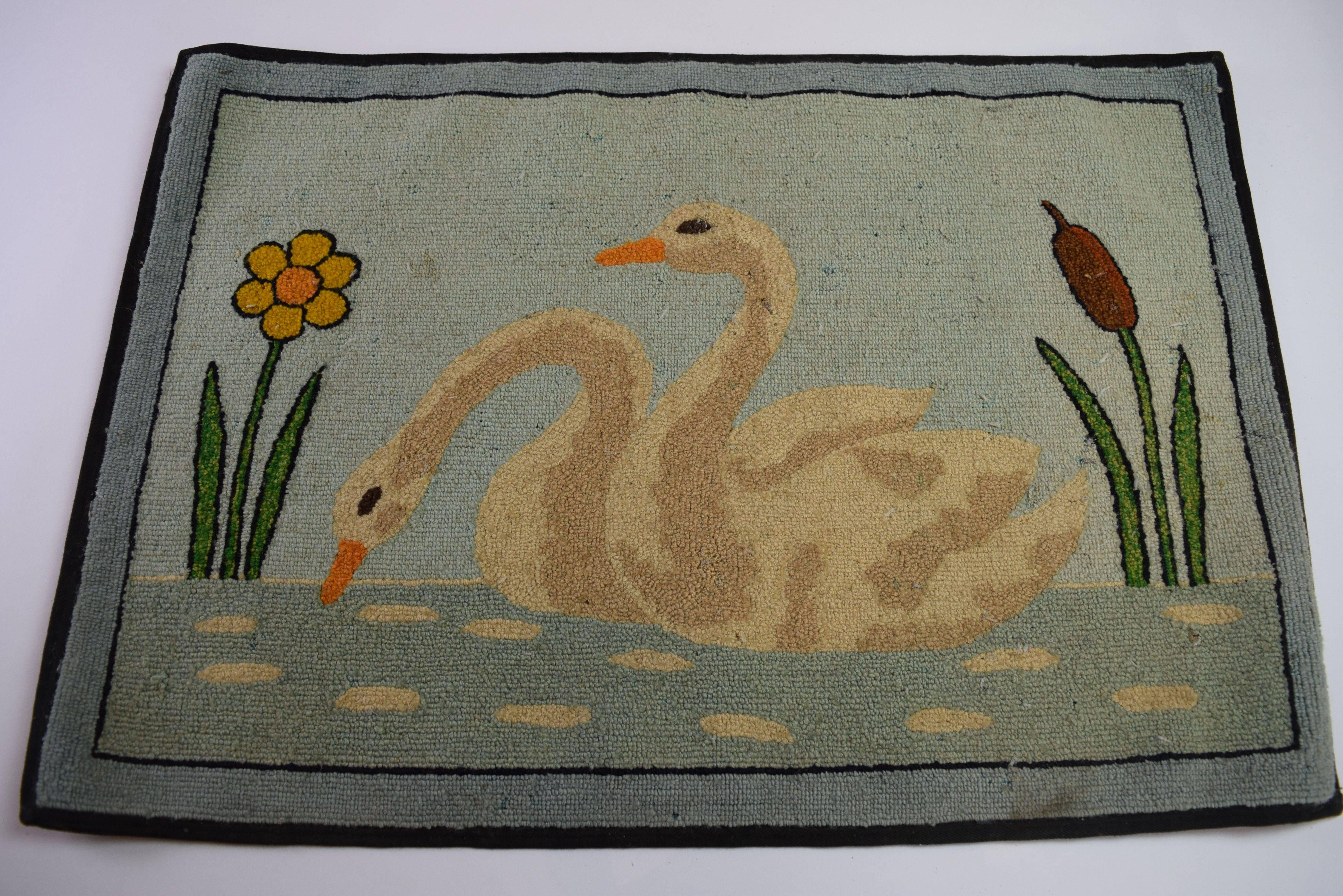 Folk Art hooked mat of a pair of swans on water flanked by a flower and reed.