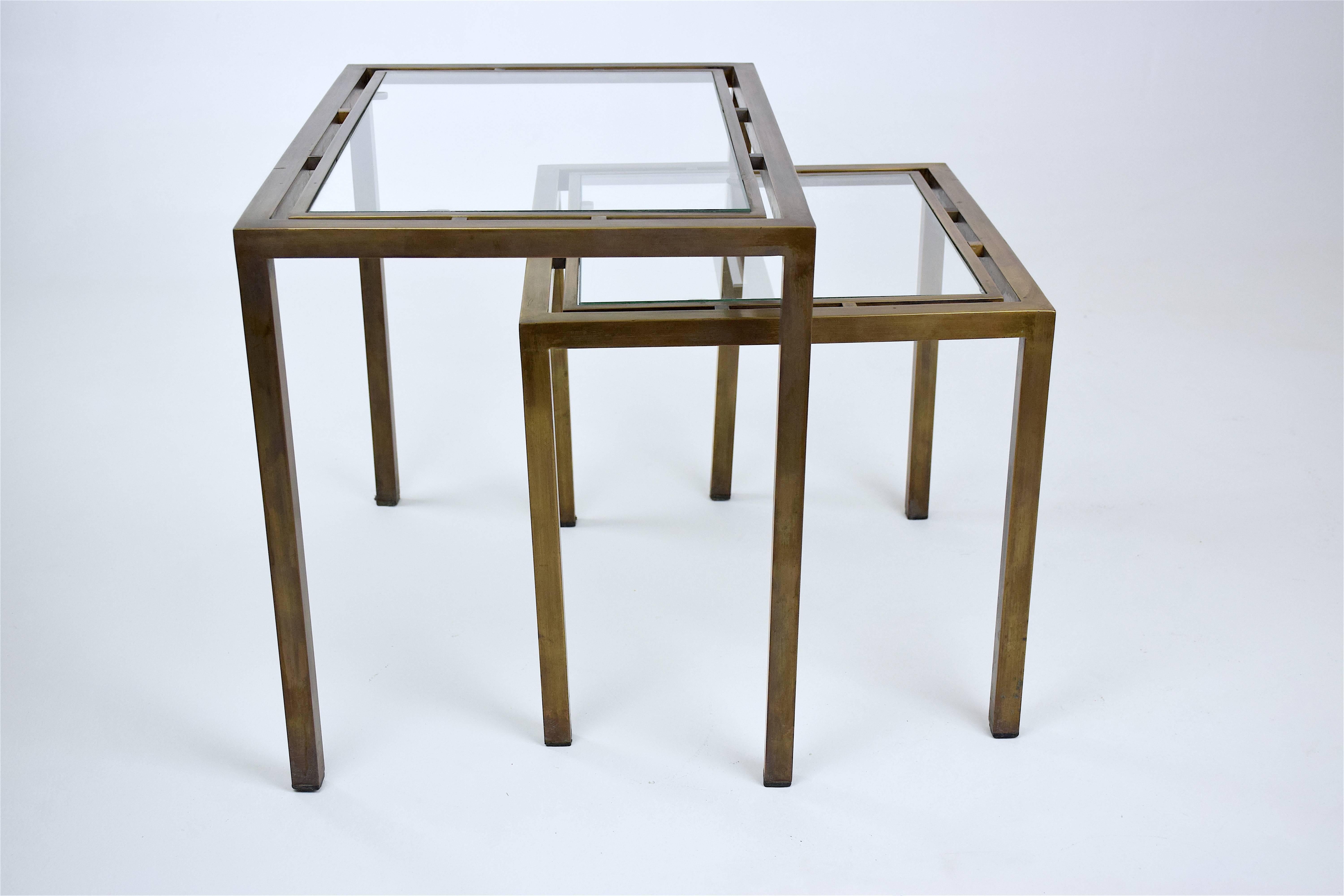 Graphic set of two 20th century vintage Mid-Century Modern nesting, side, end or coffee tables composed of solid aged brass and clear glass. 
Designed in France, circa 1970s. 
Measurements: 
37 x 55 x 42.5 cm
37 x 43 x 34.5 cm