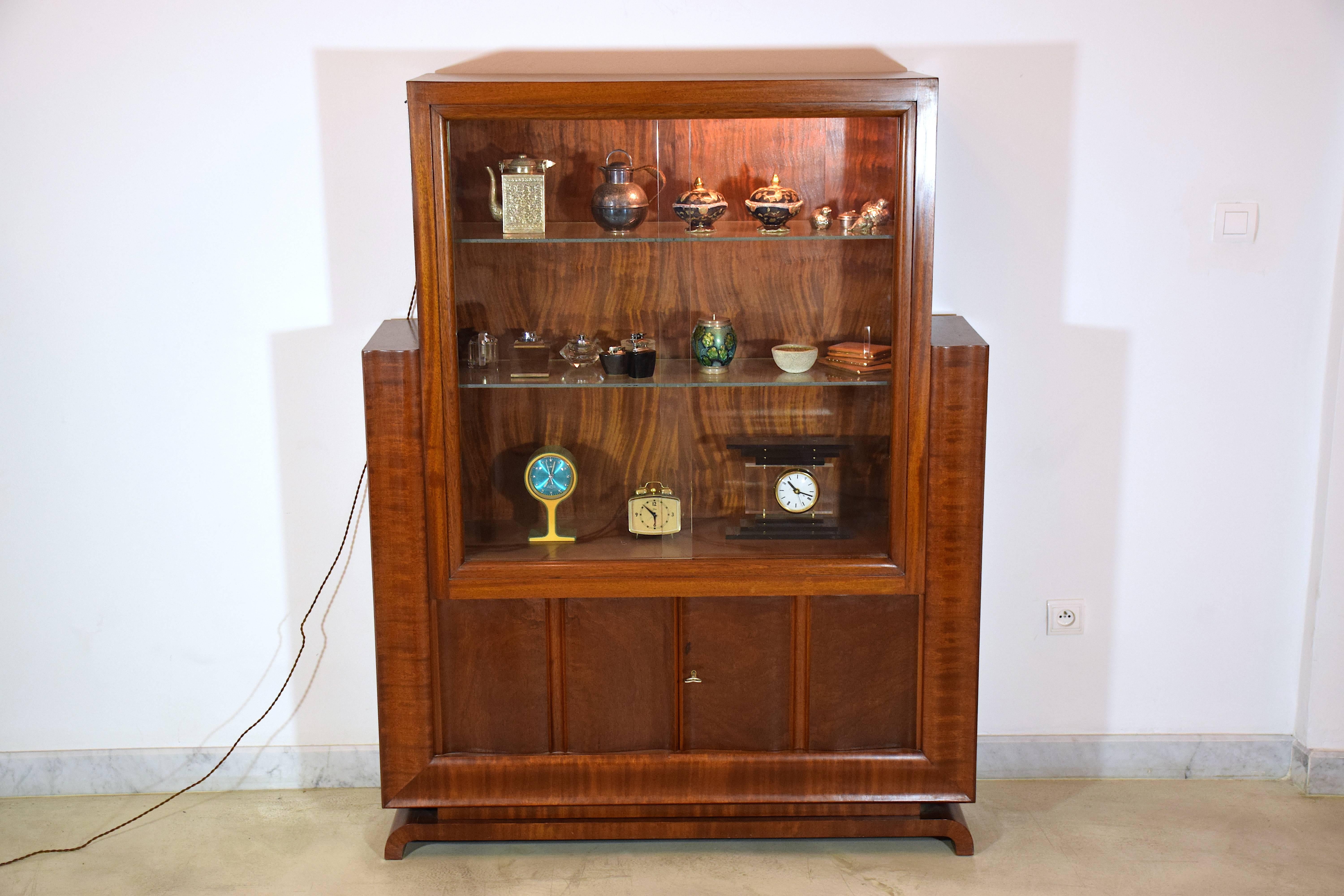  20th century vintage Art Deco light-up restored vitrine display cabinet composed of mahogany veneer, sliding glass doors and two glass shelves. The lower part is composed of a sideboard with one opening door and its original I key. 

The glass has