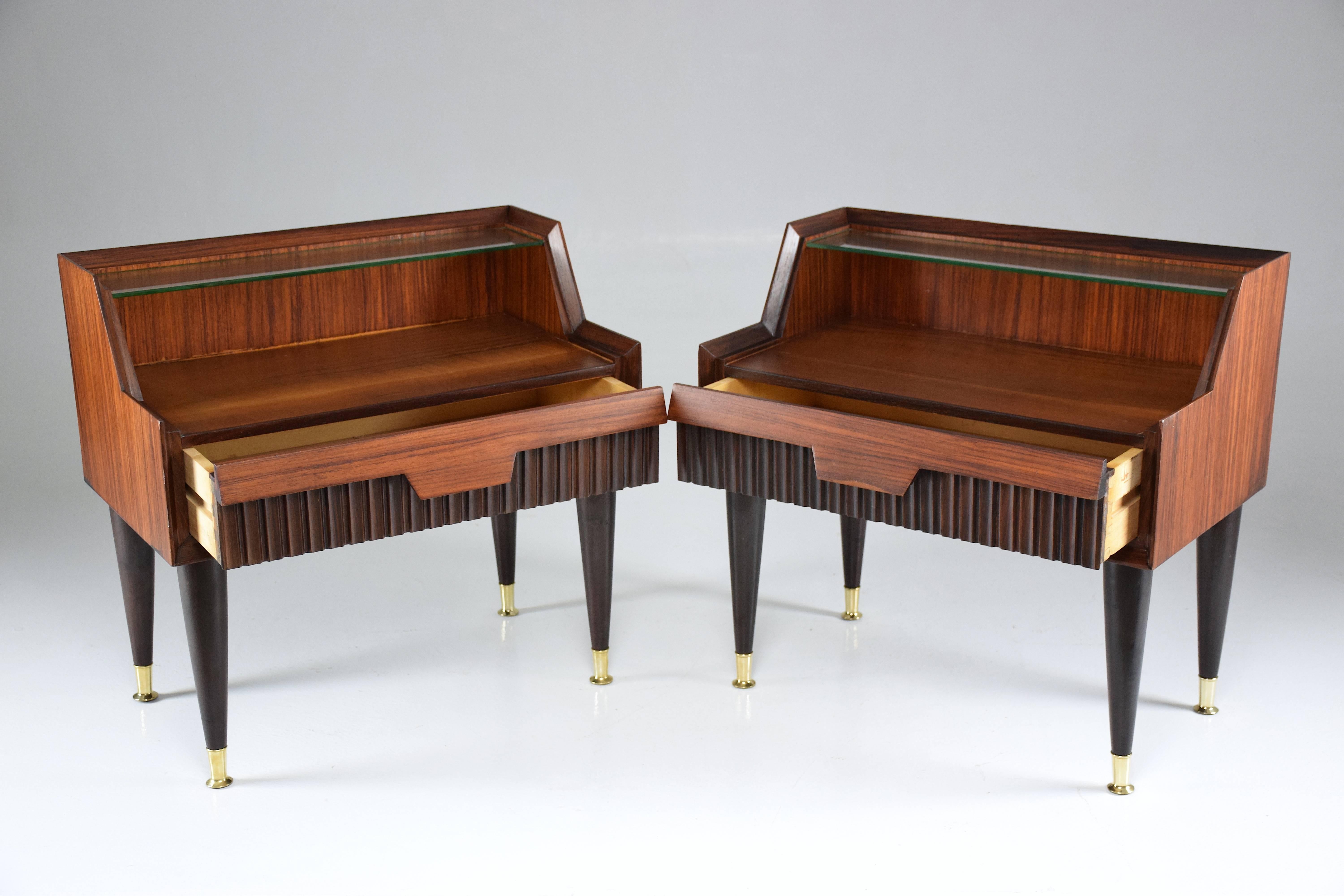 Pair of 20th century Italian vintage nightstands in fully restored condition designed in the style of a mini secretary composed of rosewood veneer, glass and polished brass endings.
These side tables are designed with a central drawer, a top glass
