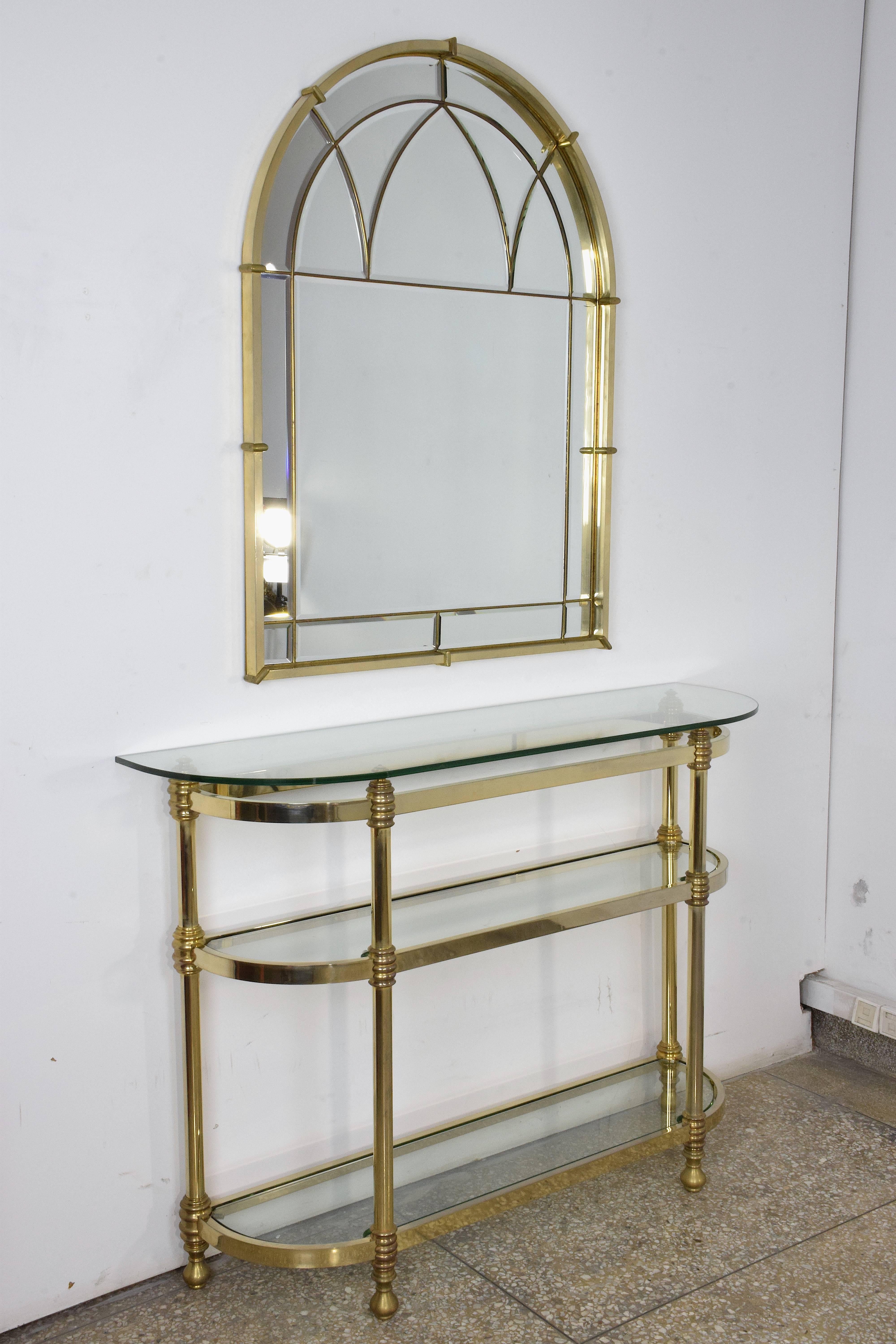 20th century vintage wall mirror and console set in hollywood regency style. The 16 beveled mirrors are joined by solid varnished brass to form beautiful curves and arches. The polished brass console table is designed with three glass shelves.