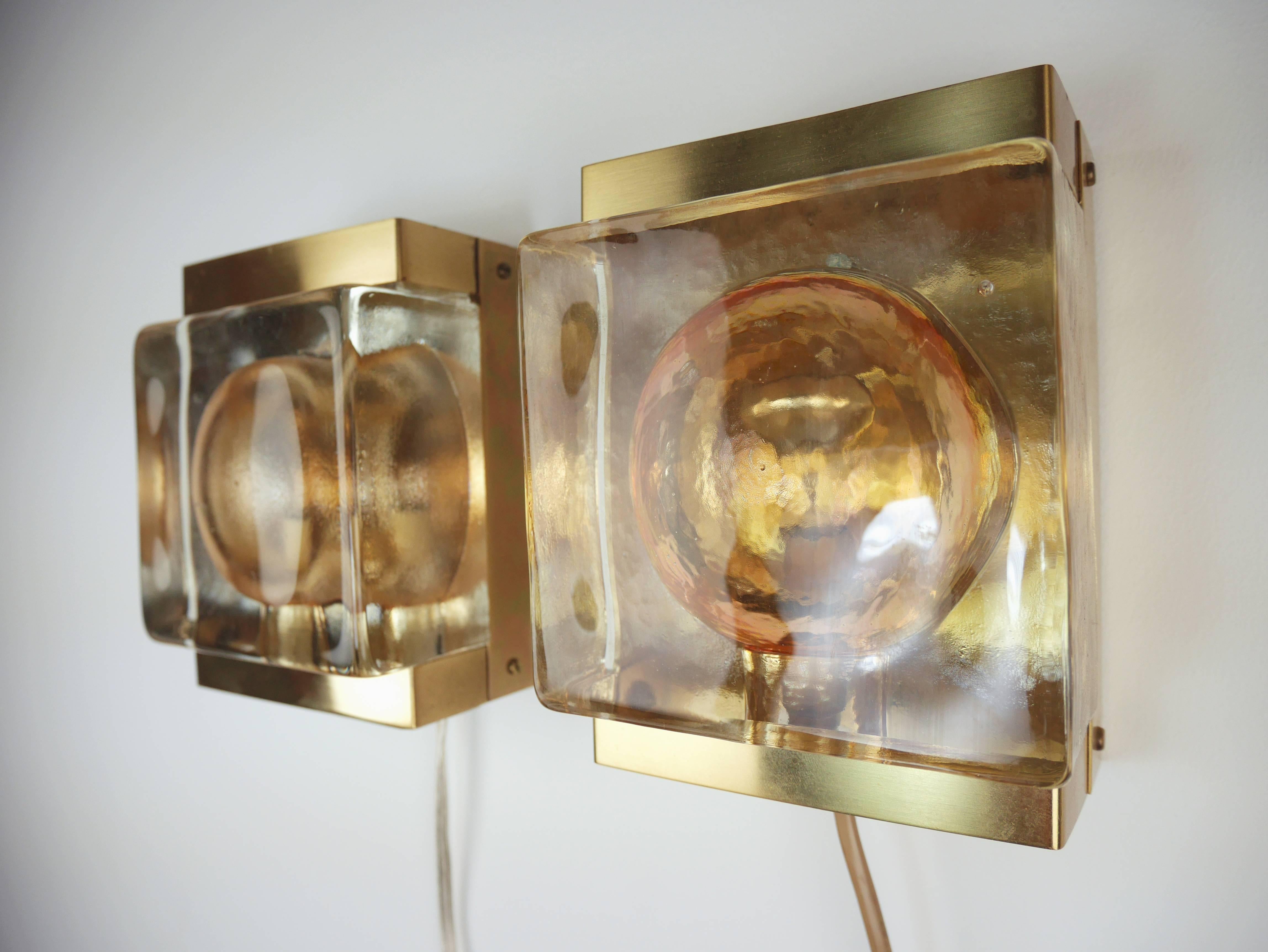 Exceptional handmade 1960s Danish Mid Century Modern wall lights by Vitrika. A block of thick solid champagne colored glass mounted on a shiny brass plate that closes around the top and bottom of the glass. The items are handmade so small
