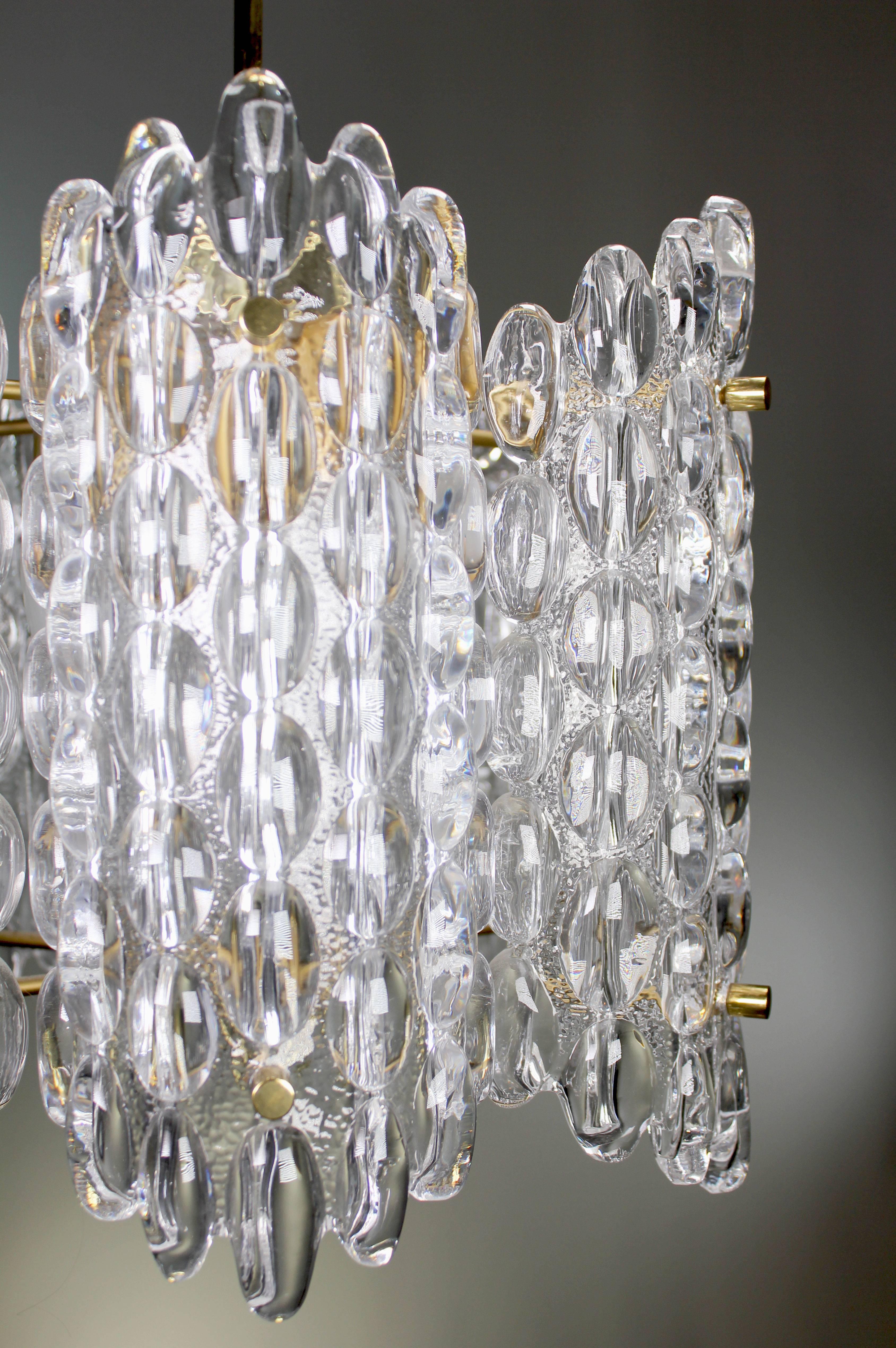 Three large iconic Swedish Mid Century Modern Orrefors chandeliers with six curved plates of bubble textured smooth clear crystal mounted on brass dividers. Original polished brass hardware, chain and canopy. By Swedish designer Carl Fagerlund for