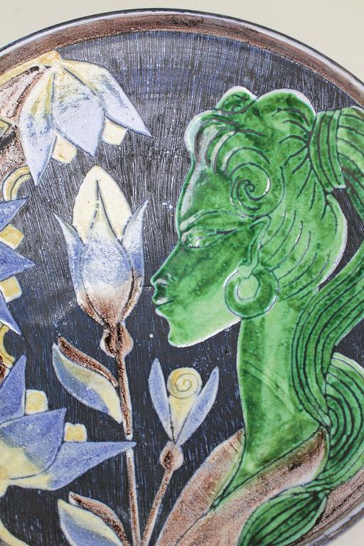 Extraordinary modernist item by Swedish Tilgmans Keramik. Fully glazed centerpiece or wall decoration depicting a green faced woman with long stemmed yellow and blue flowers on a striped dark blue background created with the sgraffito technique.