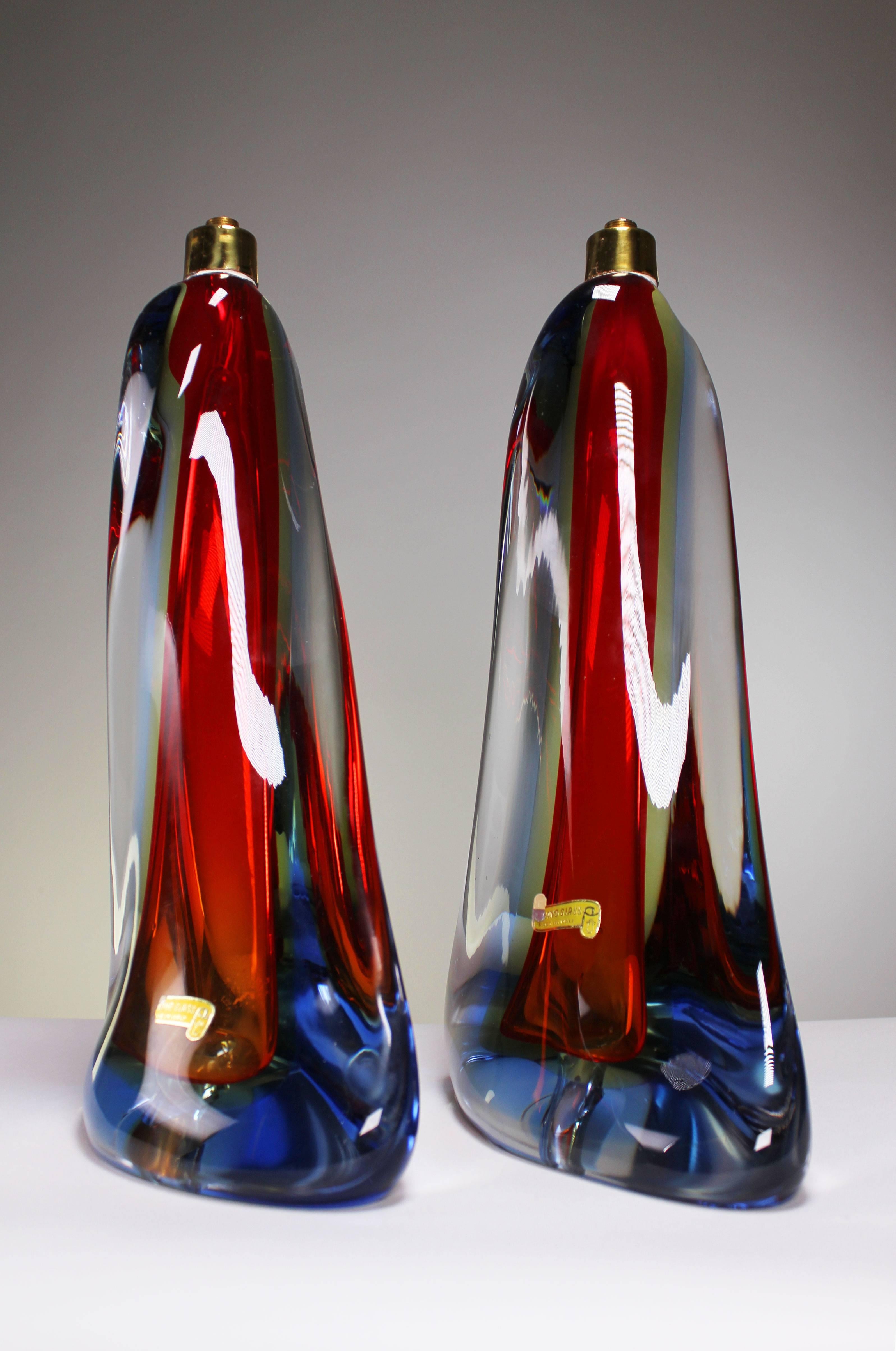 A rarely seen elegant pair of swirling Murano Sommerso table lamps that appear to be dancing with each other when standing side by side. The swirl from top to bottom is of deep red, yellow and blue crystal encased in clear crystal. Brass top.
