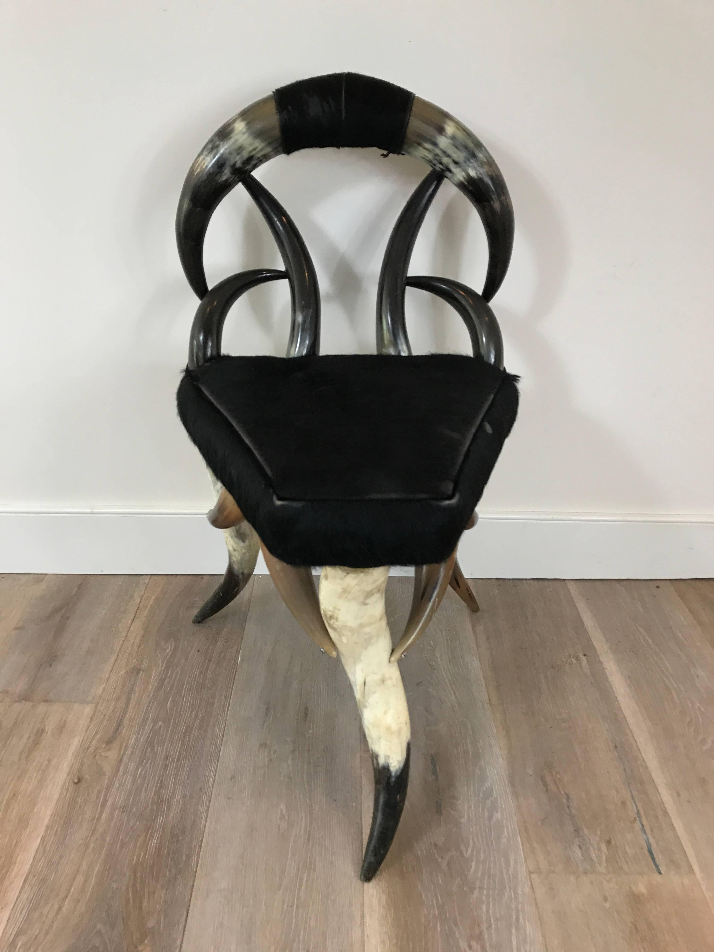 Diminutive seat constructed of steer horn with black cowhide upholstery.