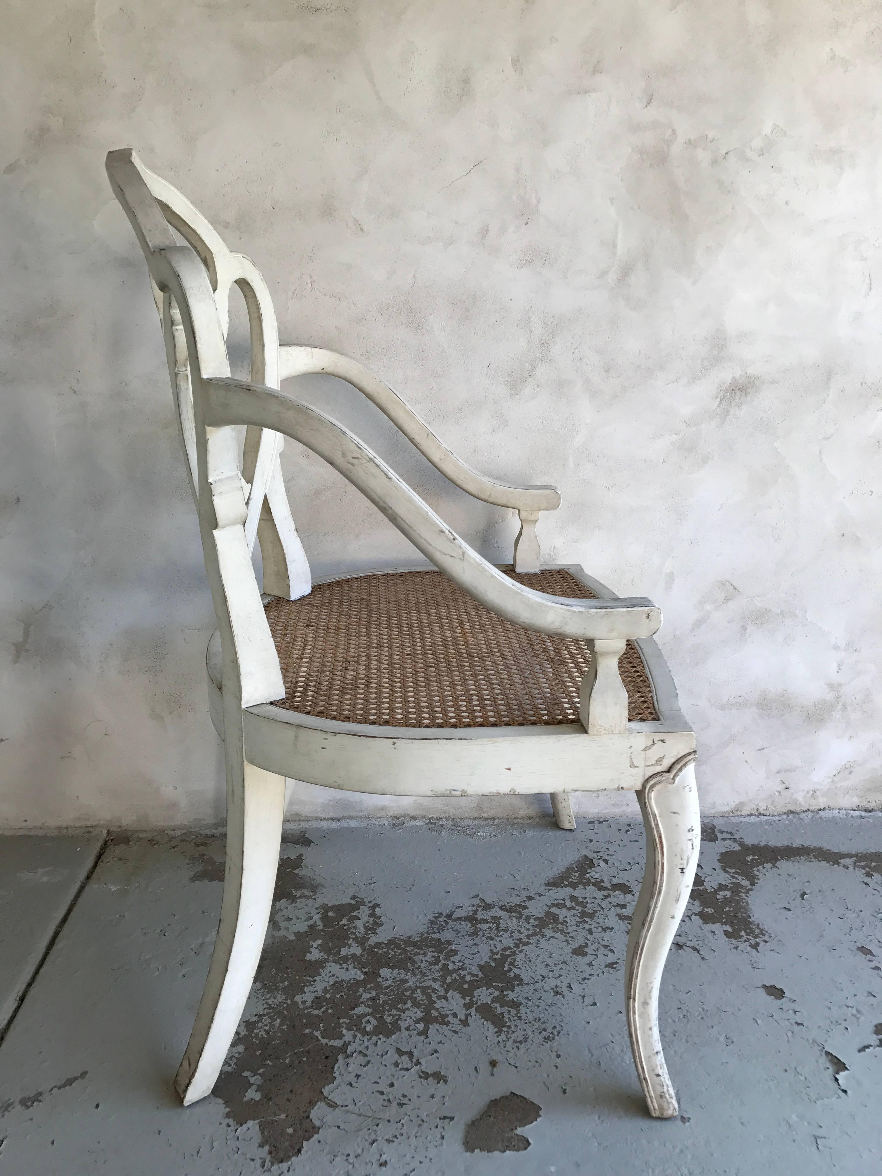 A pair of white washed armchairs with shield backrest and cane seats.