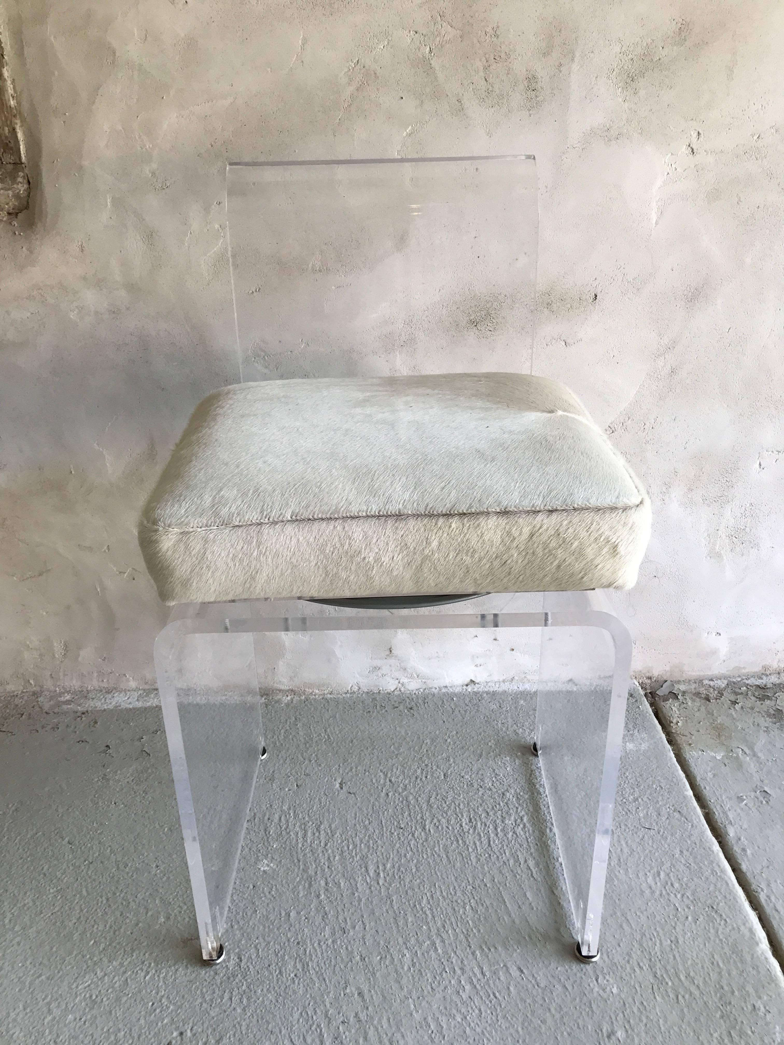 A diminutive Lucite vanity stool with swiveling off white colored hide seat.