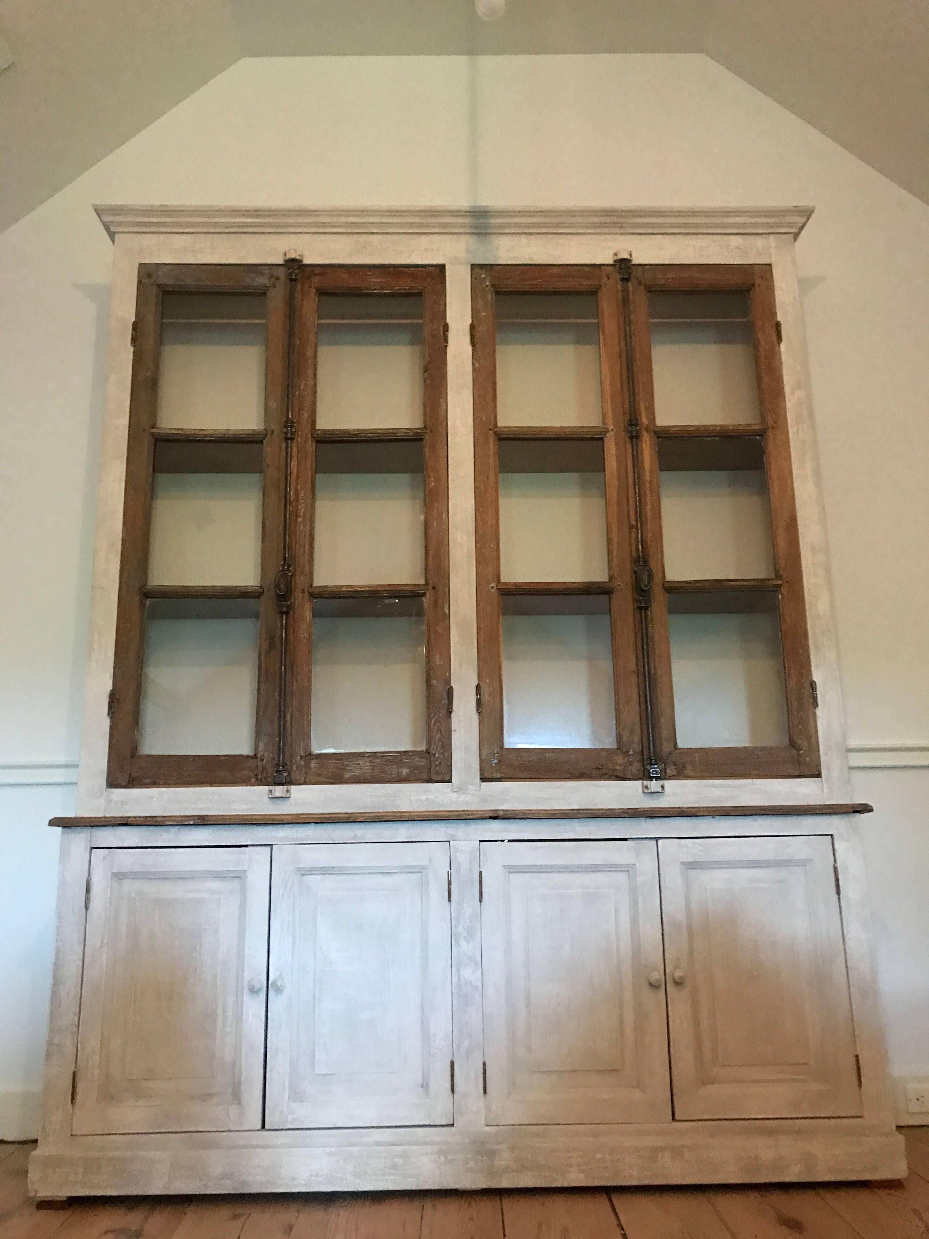 A two part French Provincial cabinet. Lower compartment have two double doors and interior shelves and the upper portion with shelving closed by two pairs of antique doors. Wonderful custom made piece repurposing antique hardware and doors. 
