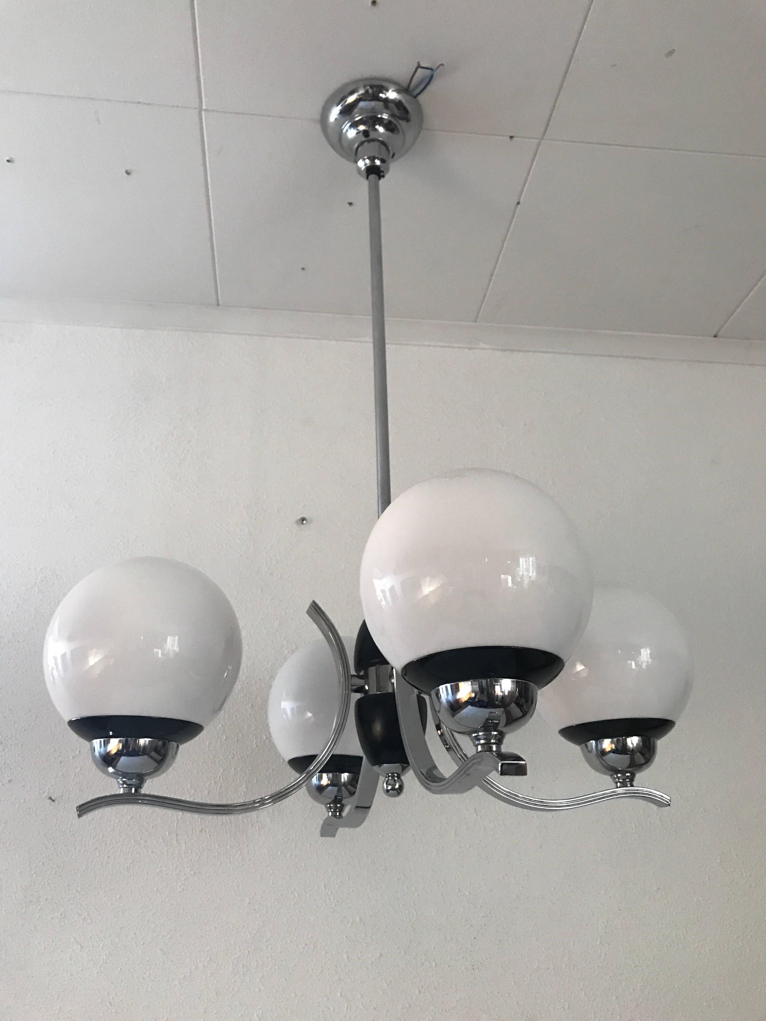 Swedish 1935 Art Deco chrome and glass four-bulb chandelier.
A beautiful chandelier made of chrome steel, black painted wood details in the center, and four opal glass shades. The chandelier is in a fantastic condition without any damages or flaws.