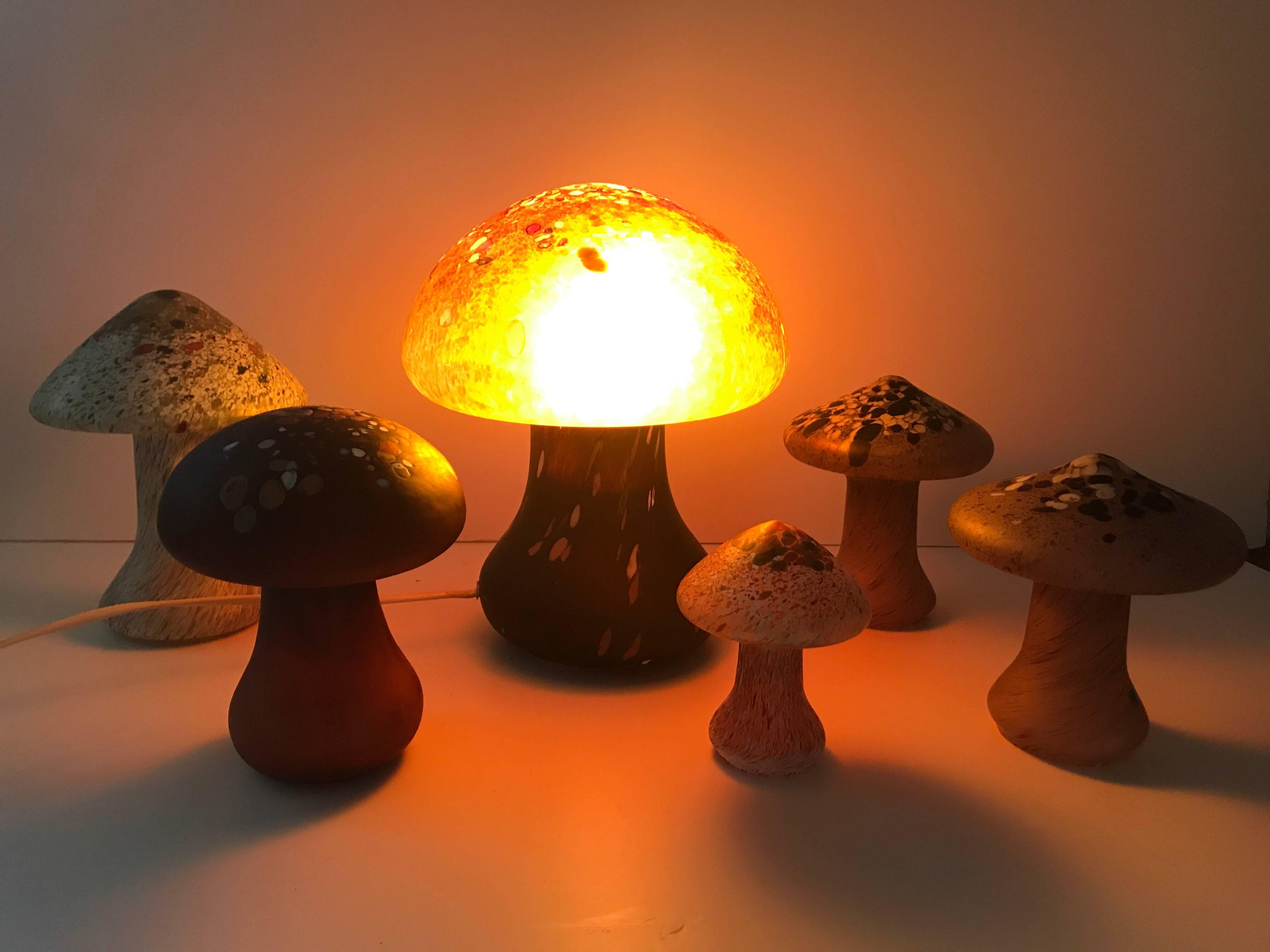 A group Swedish blown glass mushrooms and a table lamp made by Monica Bäckström in the 1970s. The mushrooms are made of blown art glass and are all individual pieces and differ in size and height. The biggest mushroom is a table lamp and measures