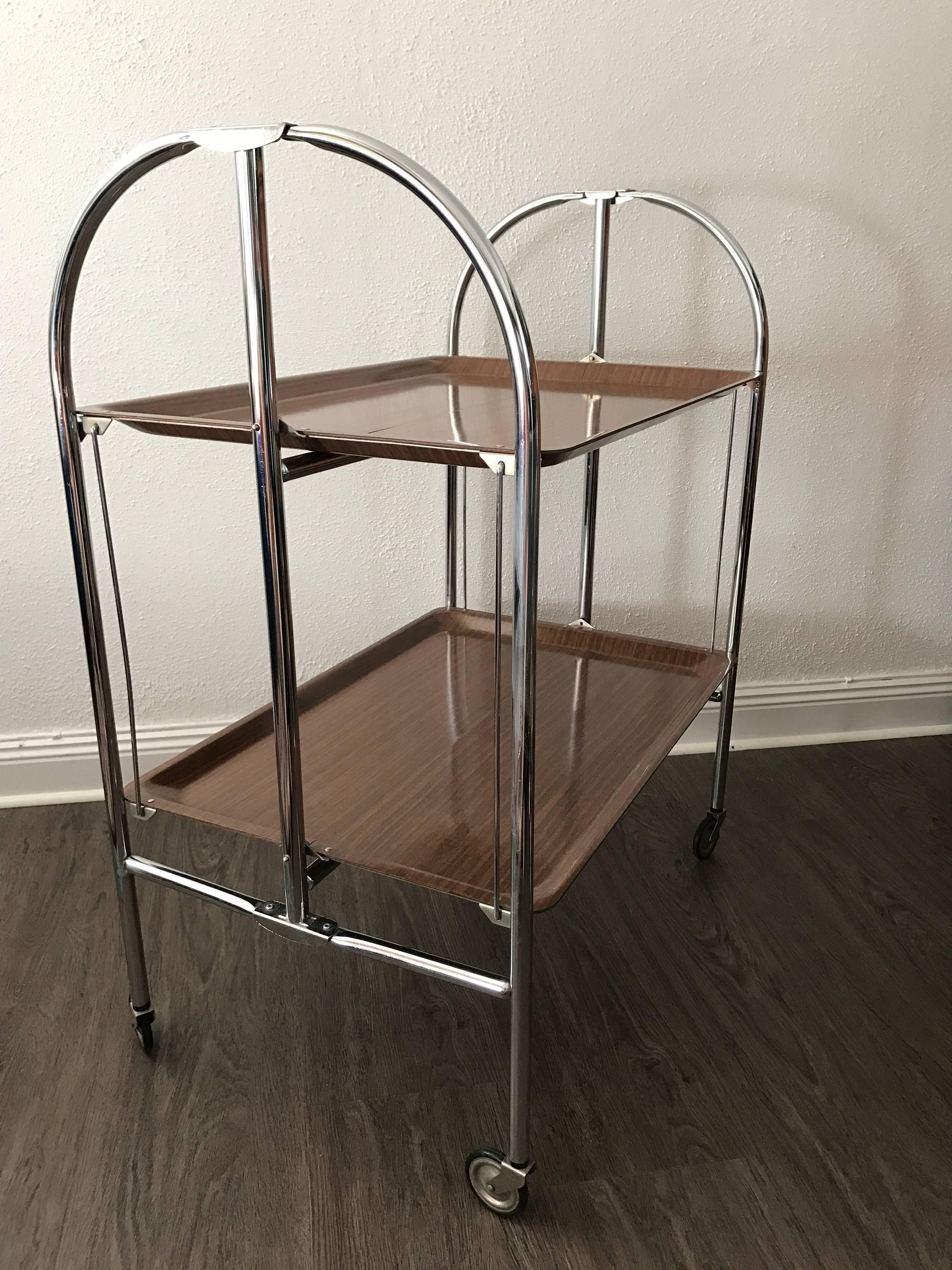 1950 Swedish chrome and laminate folding serving cart.
A very smart and easy folding serving cart in original condition, very easy to tuck away when having limited space. The trays are made of high pressure laminate and the tubes are made of chrome