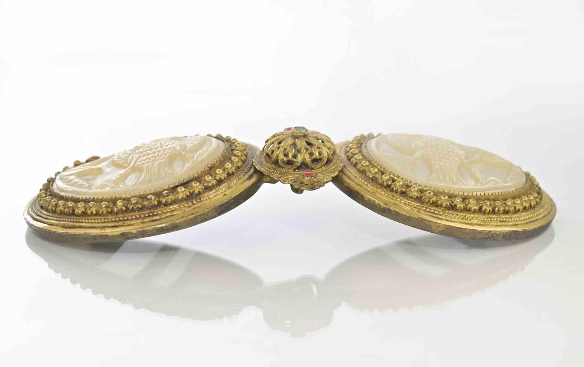 Boucle/serrure en argent doré d'Europe de l'Est, composée de deux plaques de nacre en forme d'amande, chacune placée dans un cadre de forme correspondante, les bords étant tournés vers le haut.

Finement sculptée, elle porte en son centre une pierre