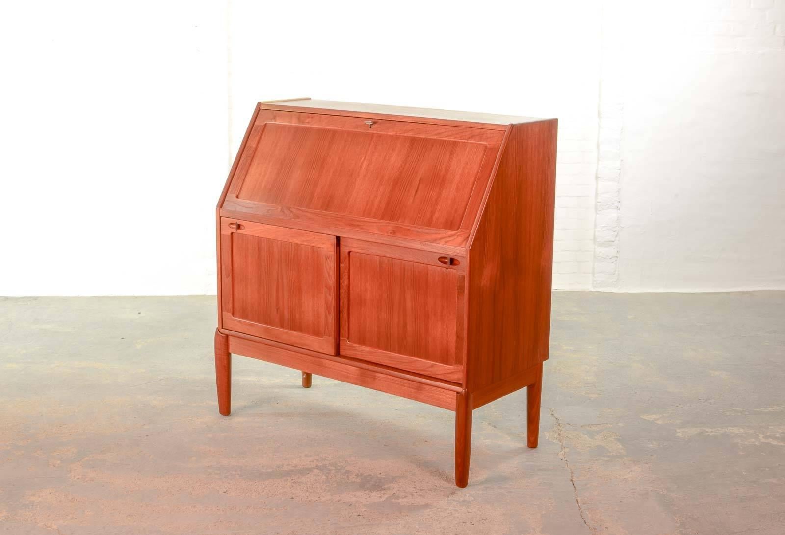 This beautiful high quality finished Danish compact writing desk cabinet is designed by H.W. Klein for Bramin in the 1960s. It features an extendable writing surface. The teak wooden structure shows an overall warm glow in its wonderful appearance