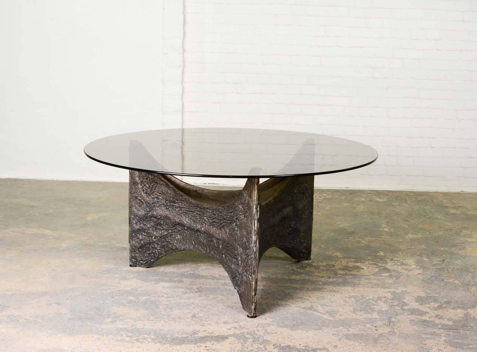 The design of this Brutalist-style coffee table is reminiscent of Paul Evans designs. The base is sculptured with an aluminium and iron alloy. The glass tabletop show some minor signs of use. Inside the framework is a lamp attached that illuminates