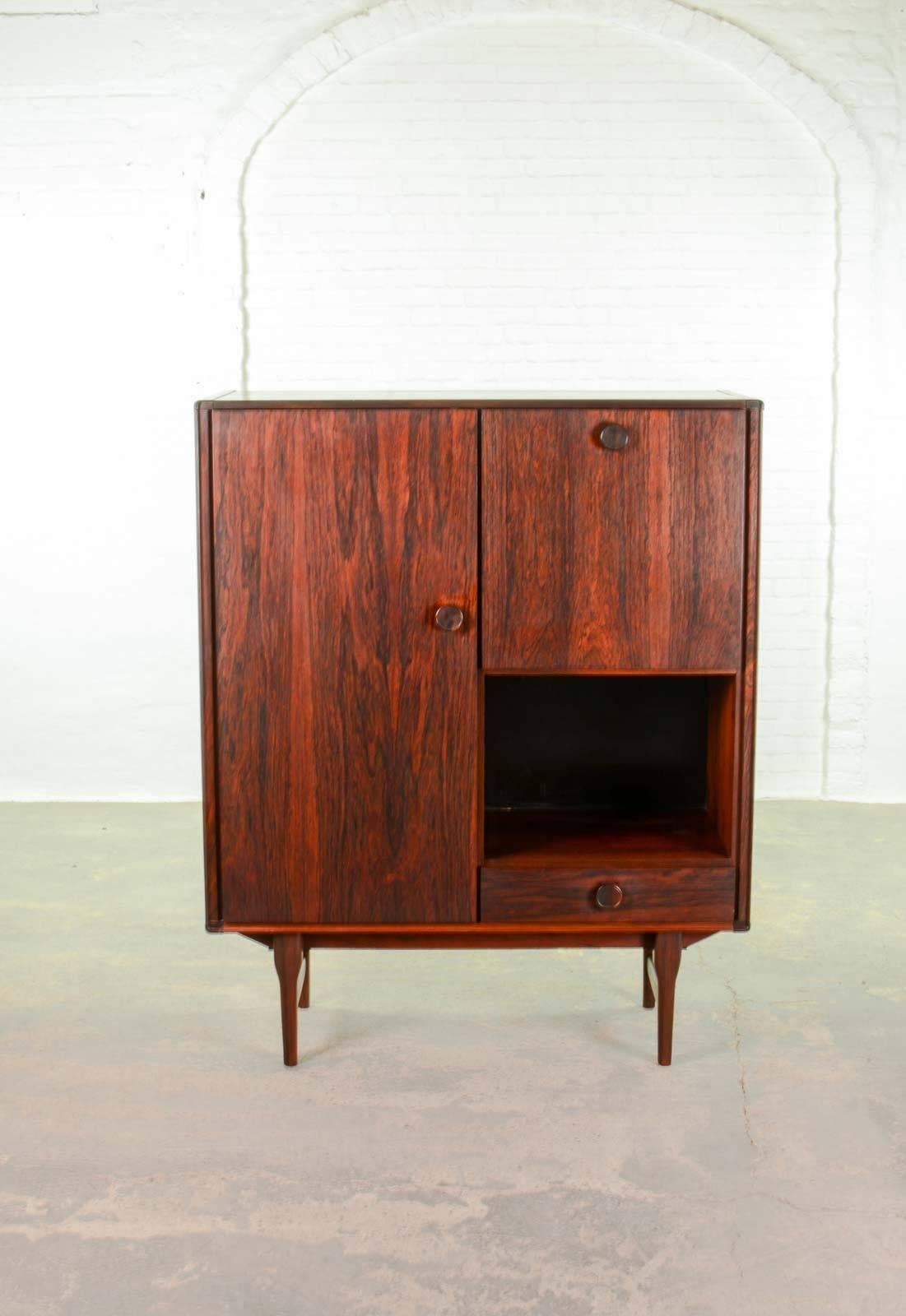 This beautiful high quality finished Dutch rosewood cabinet is made by Fristho Franeker in the 1960s. It features a tall storage compartiment with two shelves on the left side. The doors and drawer are provided with subtle detailed round rosewood