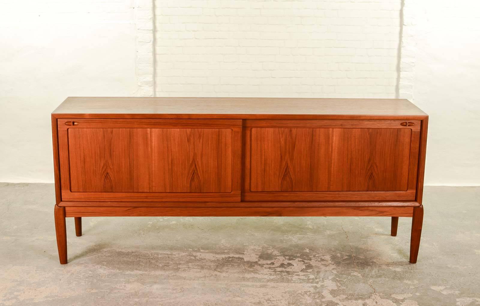 This beautiful high quality finished Mid-Century Danish sideboard or credenza is designed by H.W. Klein for Bramin in the 1960s. It features identical two sliding doors with subtle detailed teak handles. The left side contains one shelve; the right