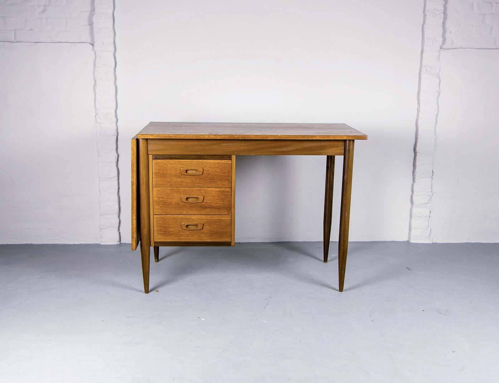 This teak writing desk was designed by Arne Vodder and was produced in Finland in the 1960s for Asko. It is made from teak and features a drop leaf on the left hand side, that, when lifted and sided extends the working space area of the desk top