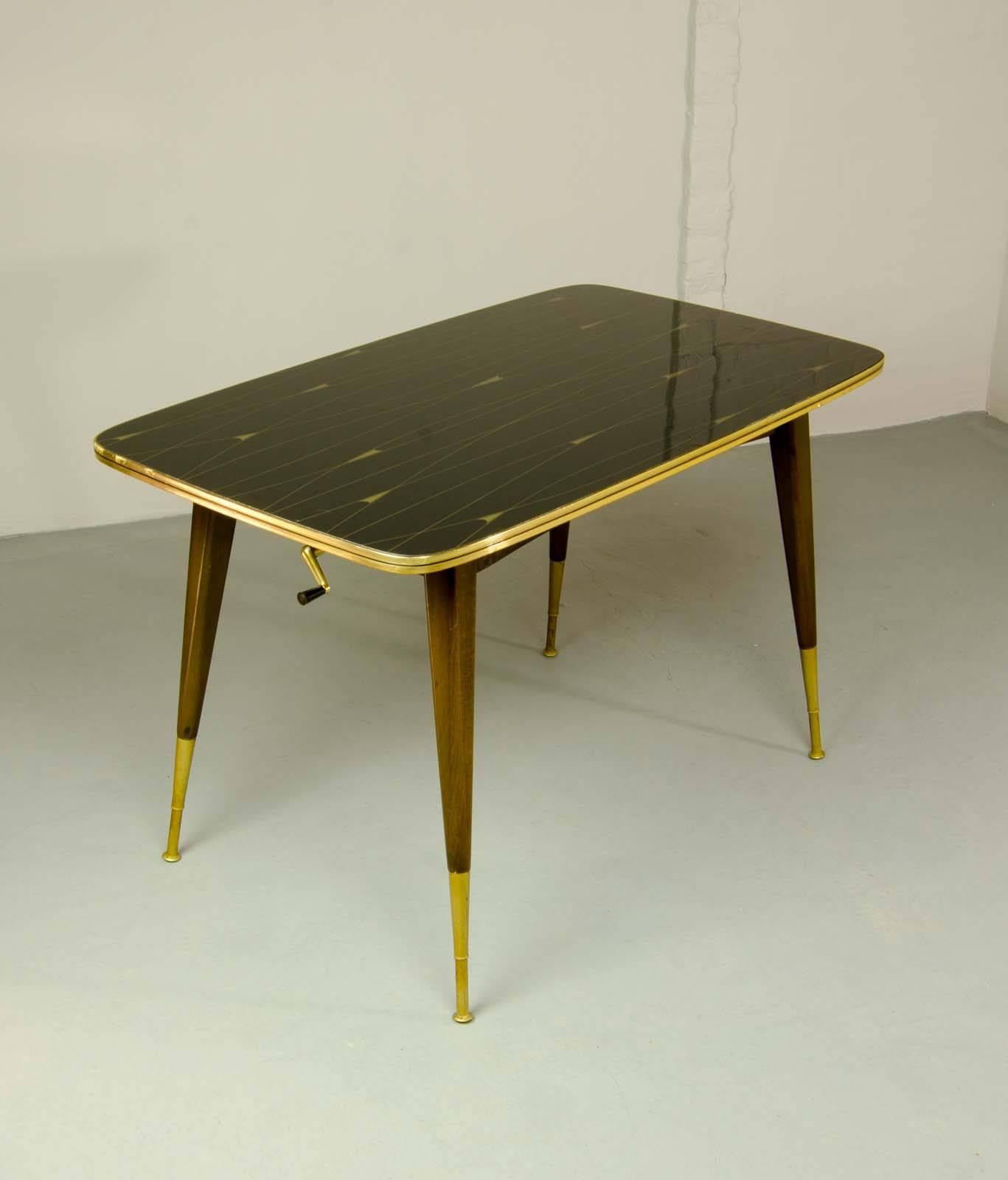 Very stylish and elegant black and brass game- / coffee table on teak wooden frame with slim brass feet. This rare table is adjustable in height by using the brass sling handle. However the designer is unknown, this unique table is probably