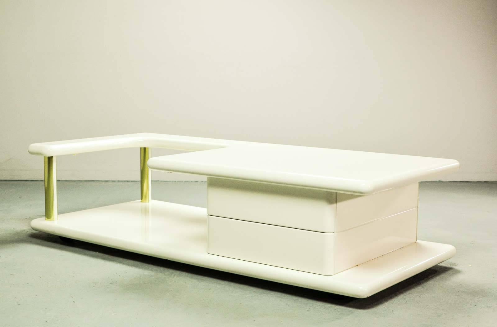 Italian white high gloss lacquered coffee table with brass elements. The table features two hidden drawers which are integrated in the design in a very elegant way. Another striking detail is the free-form shaped tabletop that enables the user to