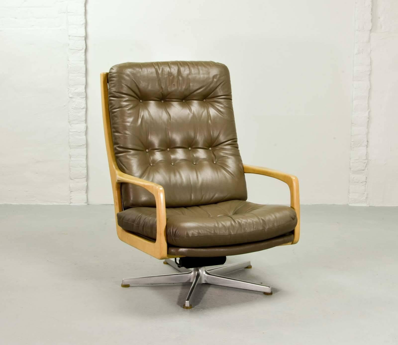 This leather swivel lounge chair originates from the 1970s and was designed by Eugen Schmidt, Germany. It is made from a fine constructed wooden frame with armrests on a stainless steel polished pedestal and features a camel brown colored leather